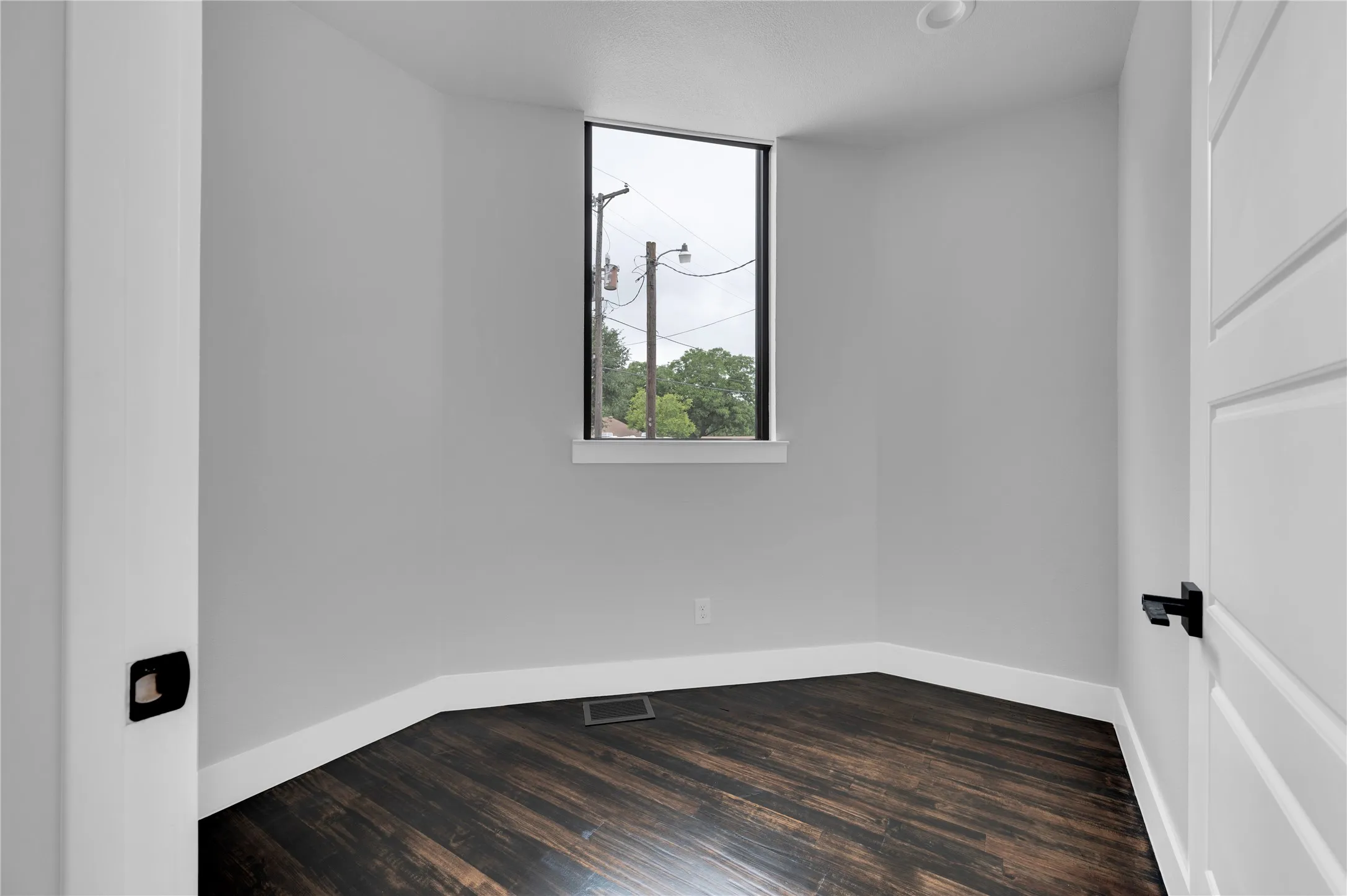 Compact room featuring dark wood-finish flooring and a single rectangular window