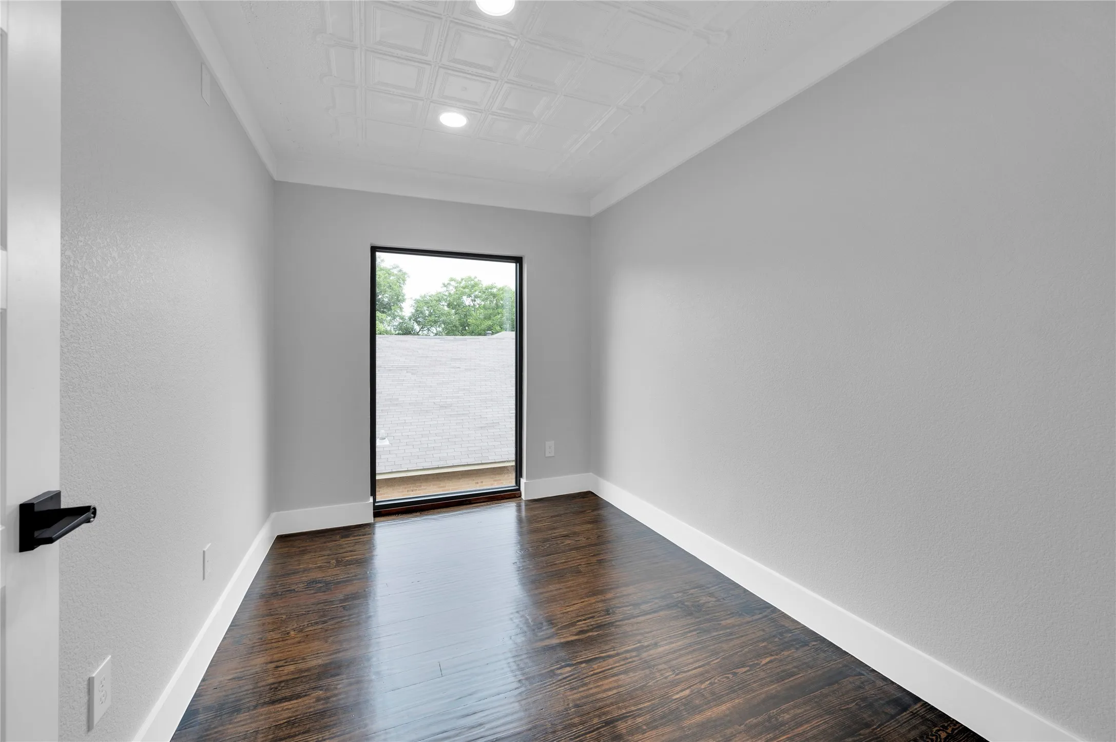 Room featuring a large black-framed window, dark wood-finish flooring, and light gray painted walls