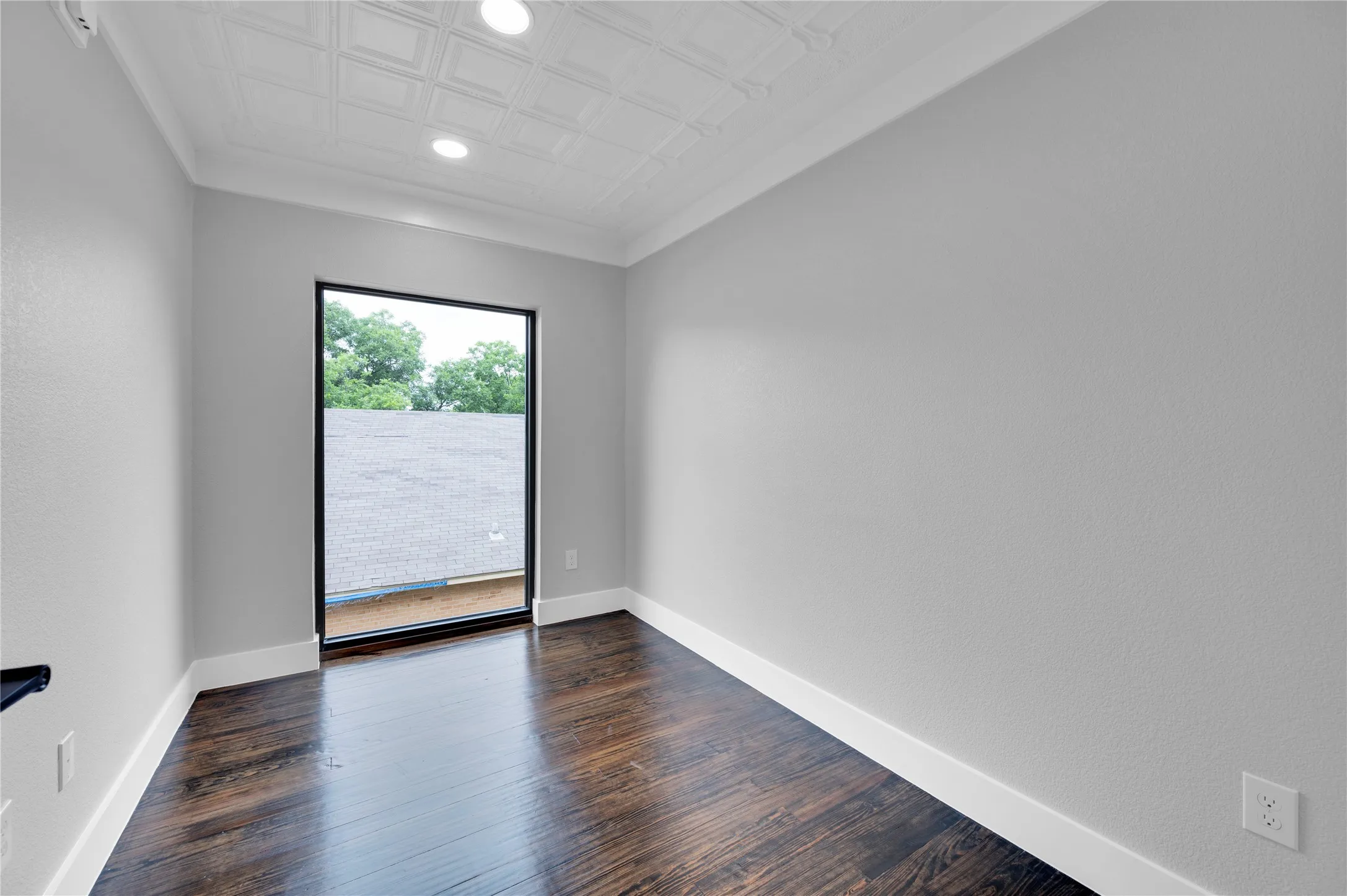 Room featuring a large black-framed window, dark wood-finish flooring, white baseboards, and light gray walls
