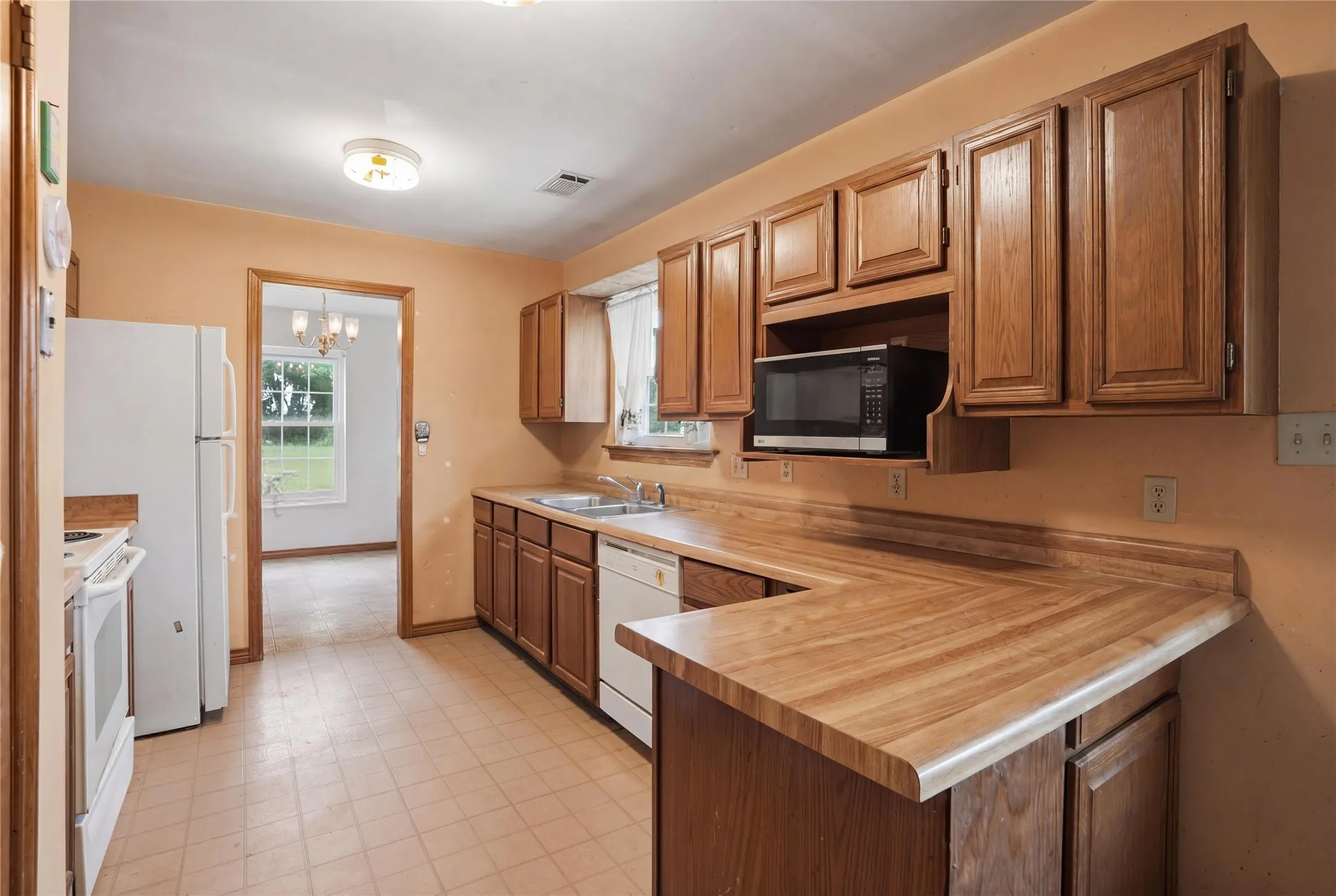 Functional kitchen showcasing wood-finish cabinets, U-shaped countertops, stainless steel sink, and light-colored flooring