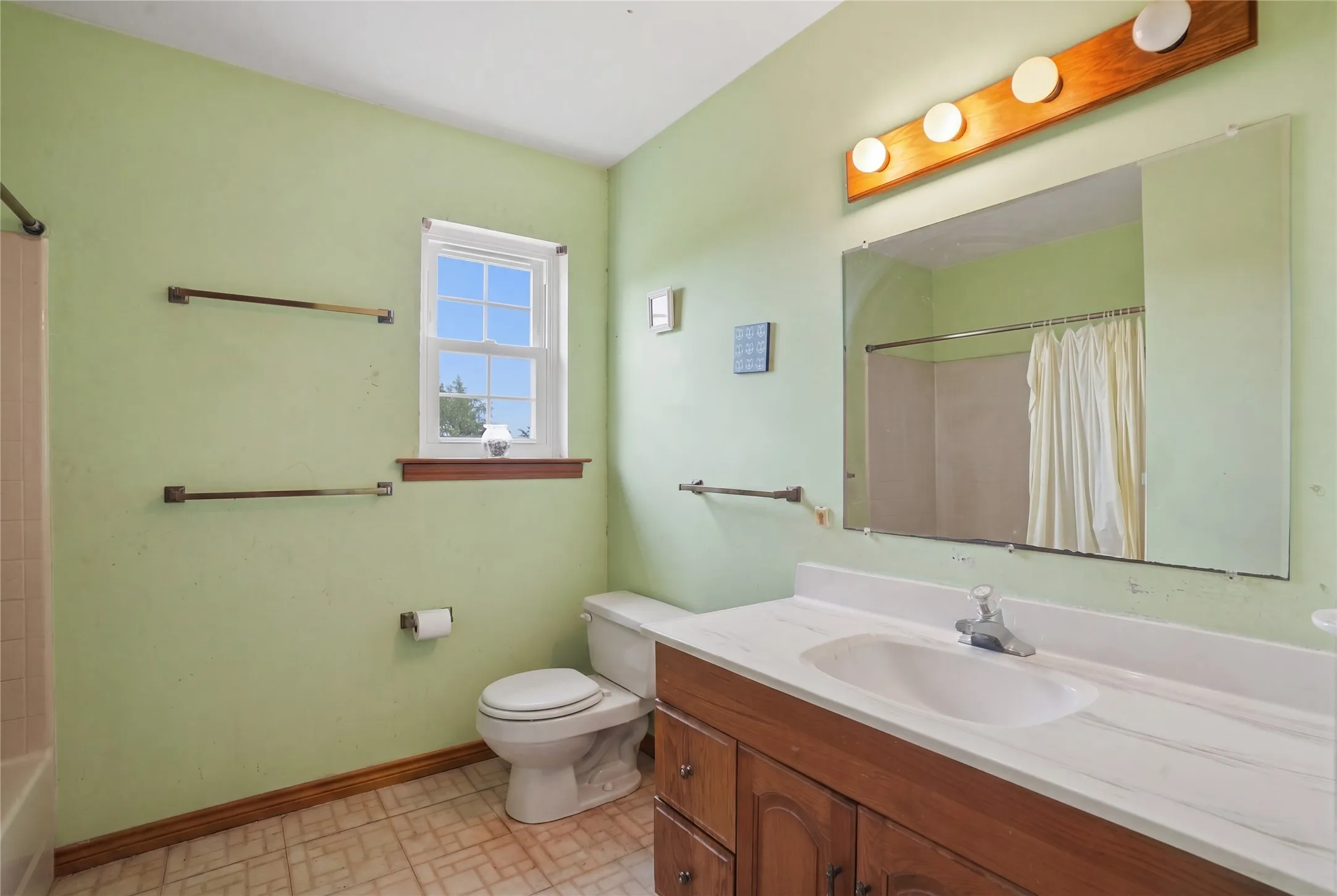 Conveniently designed bathroom complete with a generous vanity workspace, multi-bulb vanity light fixture, built-in towel bars, and a combined tub and shower area