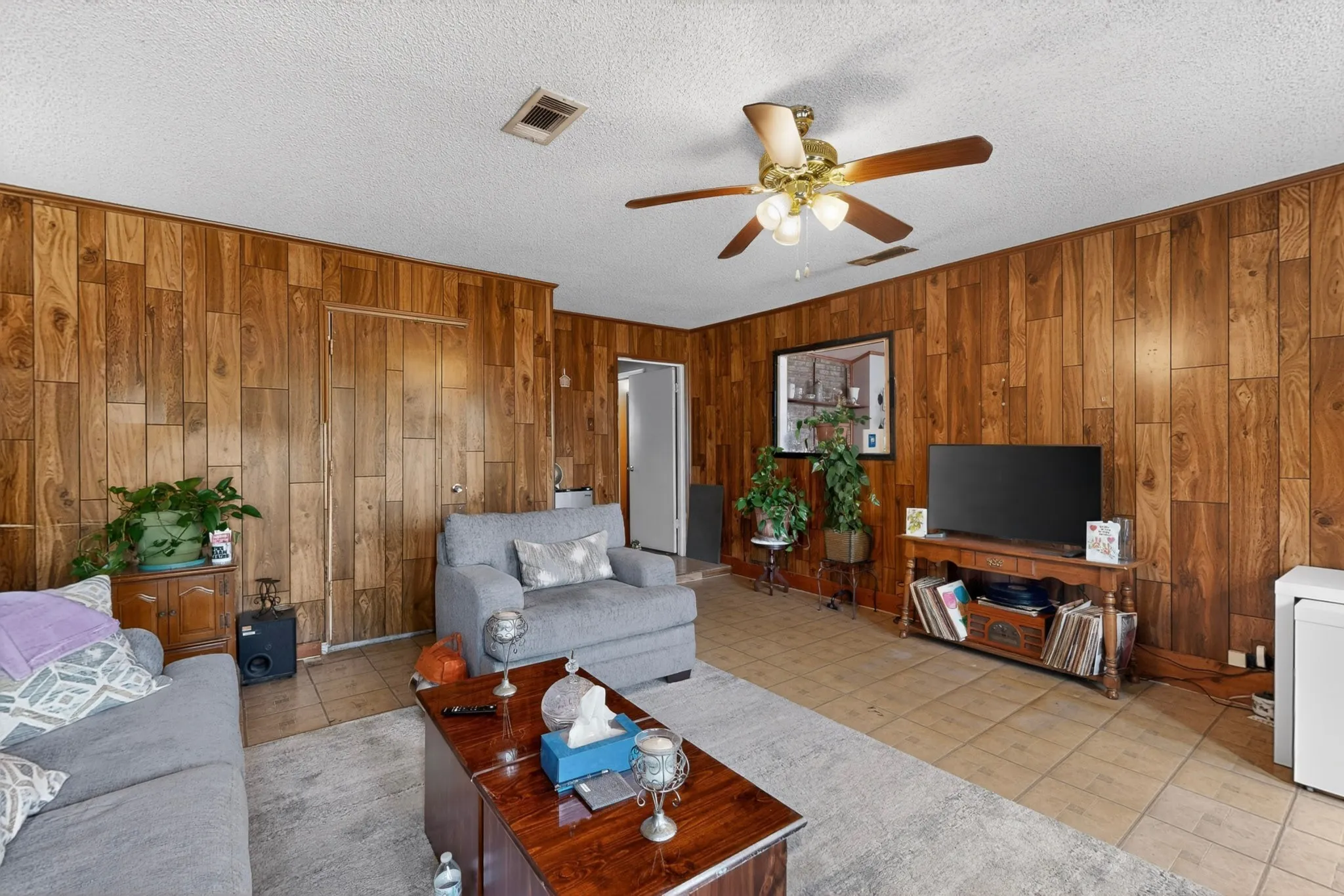 Living area featuring wood paneling throughout, a ceiling fan with integrated lighting, and tile flooring