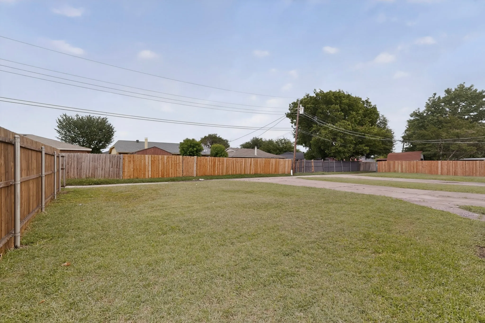 Expansive green lawn area featuring wood panel fencing, mature trees, and a gravel driveway