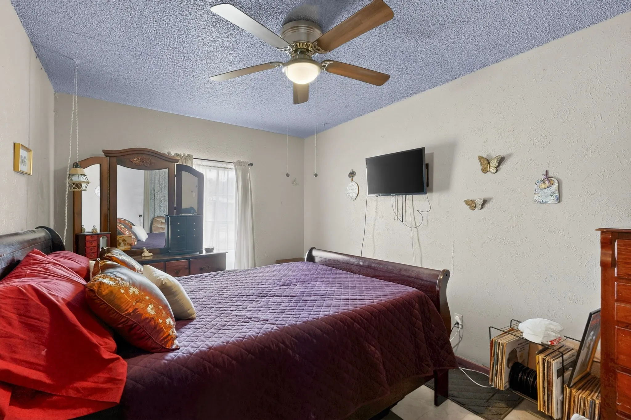 Bedroom featuring a textured ceiling with a ceiling fan, light-toned walls, and a window with white curtains