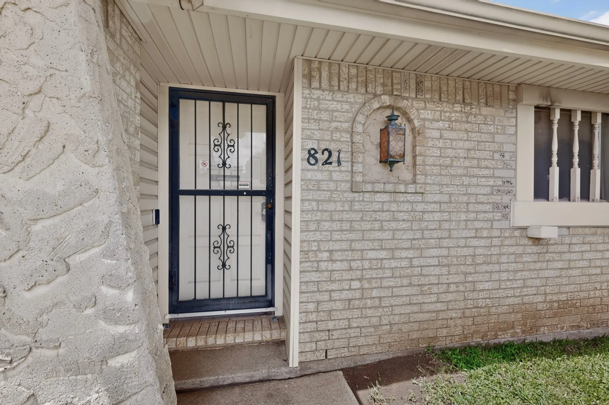 Front entry featuring a security screen door, light brick facade, and an arched wall lantern