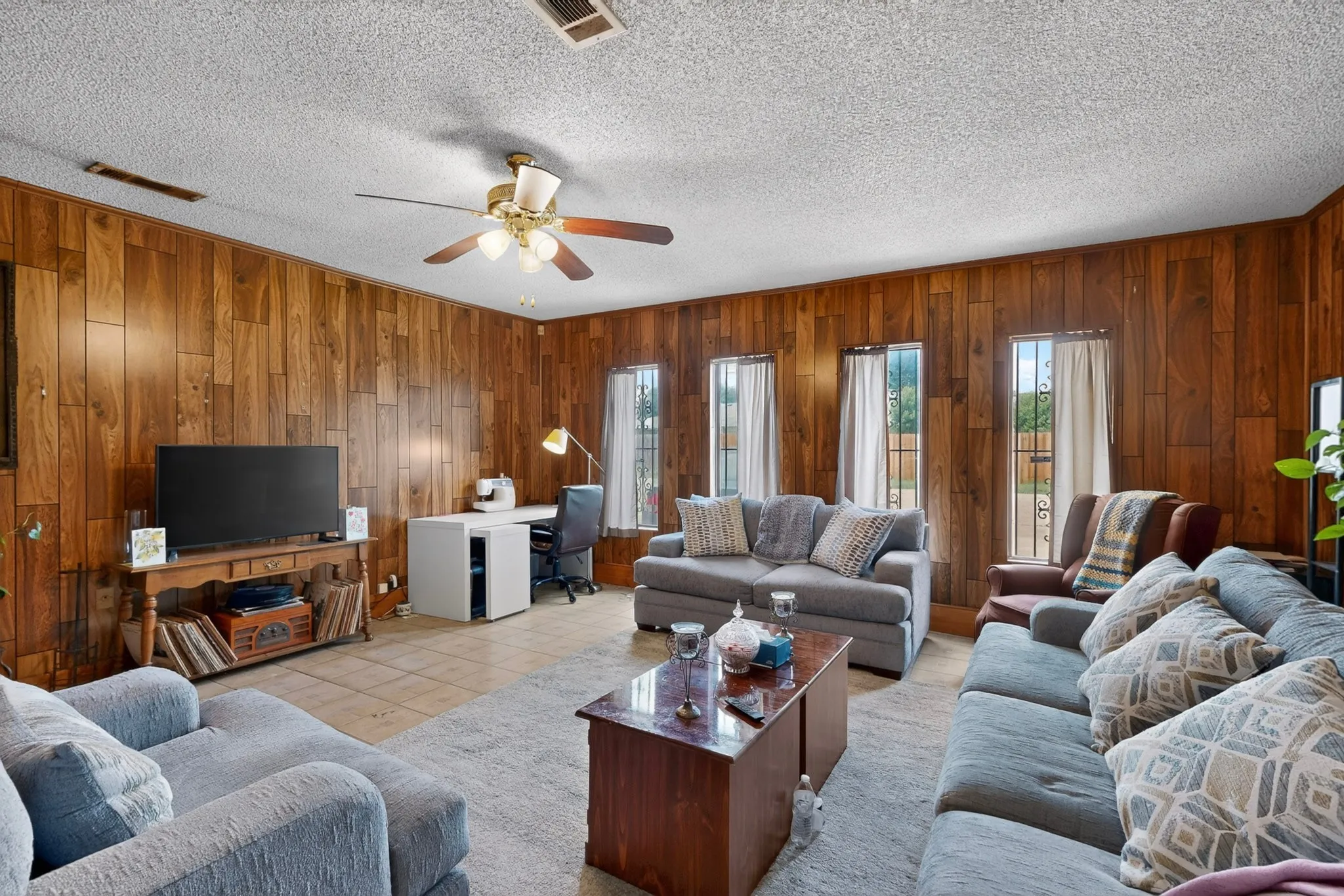 Spacious living area featuring wood-paneled walls, tile flooring, and a ceiling fan with integrated lighting