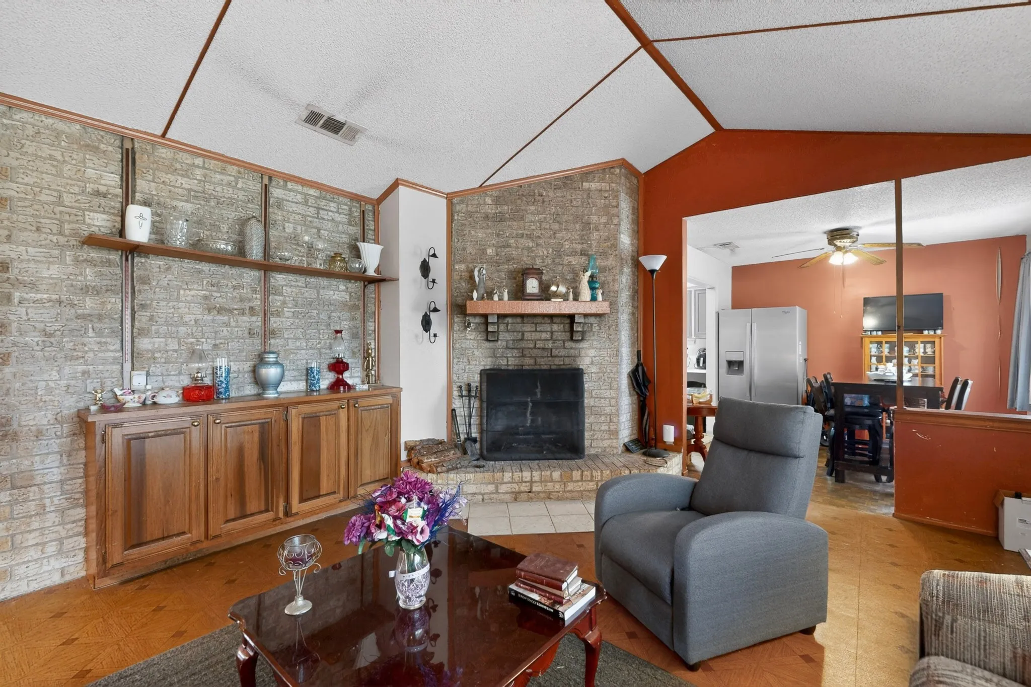 Living area featuring a brick fireplace with a wood mantel, a vaulted ceiling, wood-finish flooring, and built-in wood cabinetry with shelving