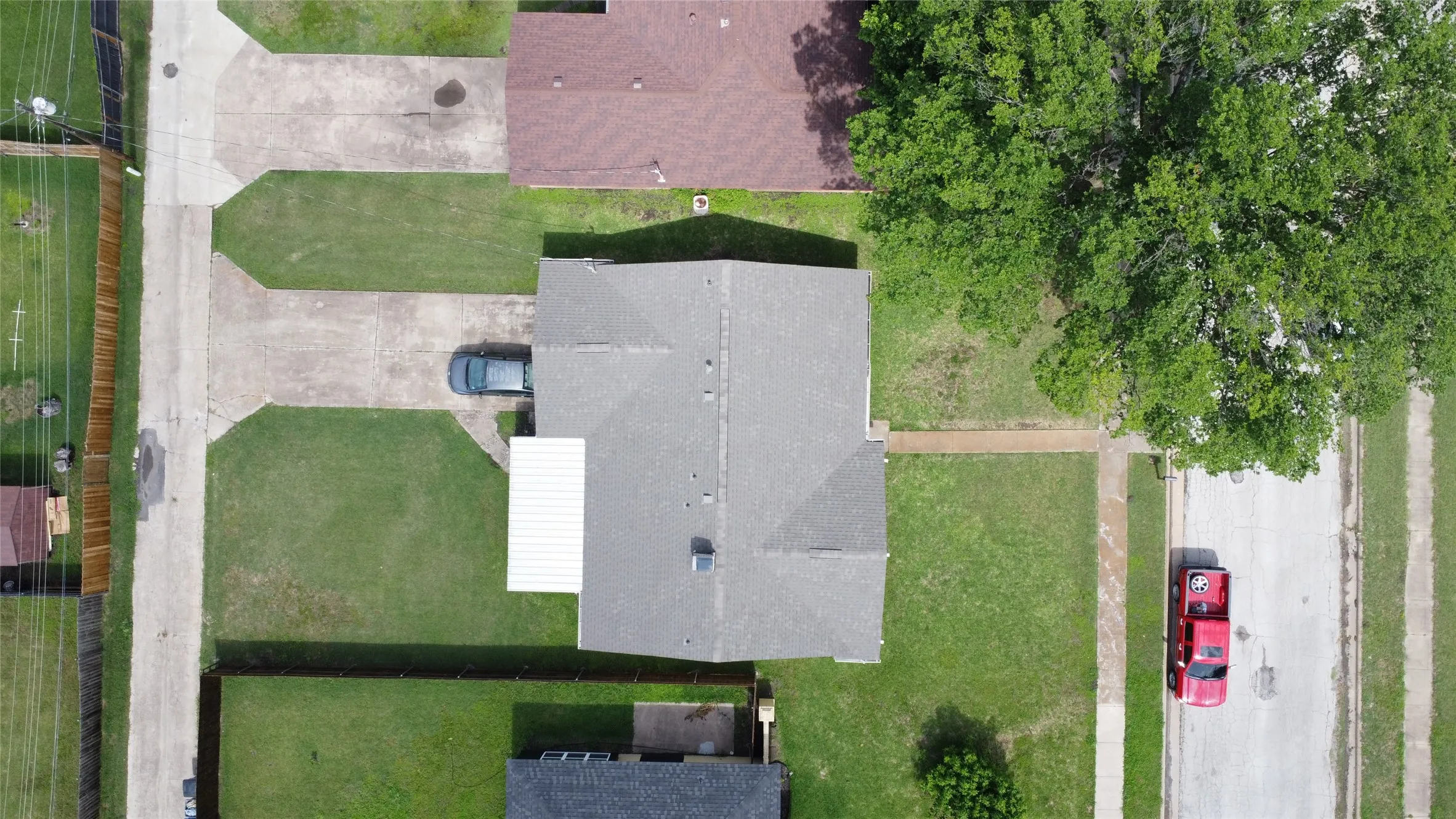 Overhead view of a residential property featuring a gray shingled roof, a covered patio structure, and a concrete driveway