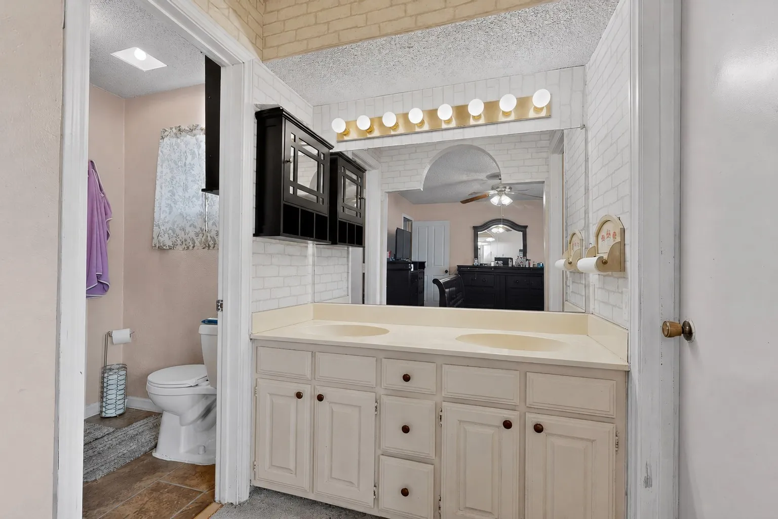 Dual vanity with integrated sinks, white cabinetry, and wall-mounted lighting