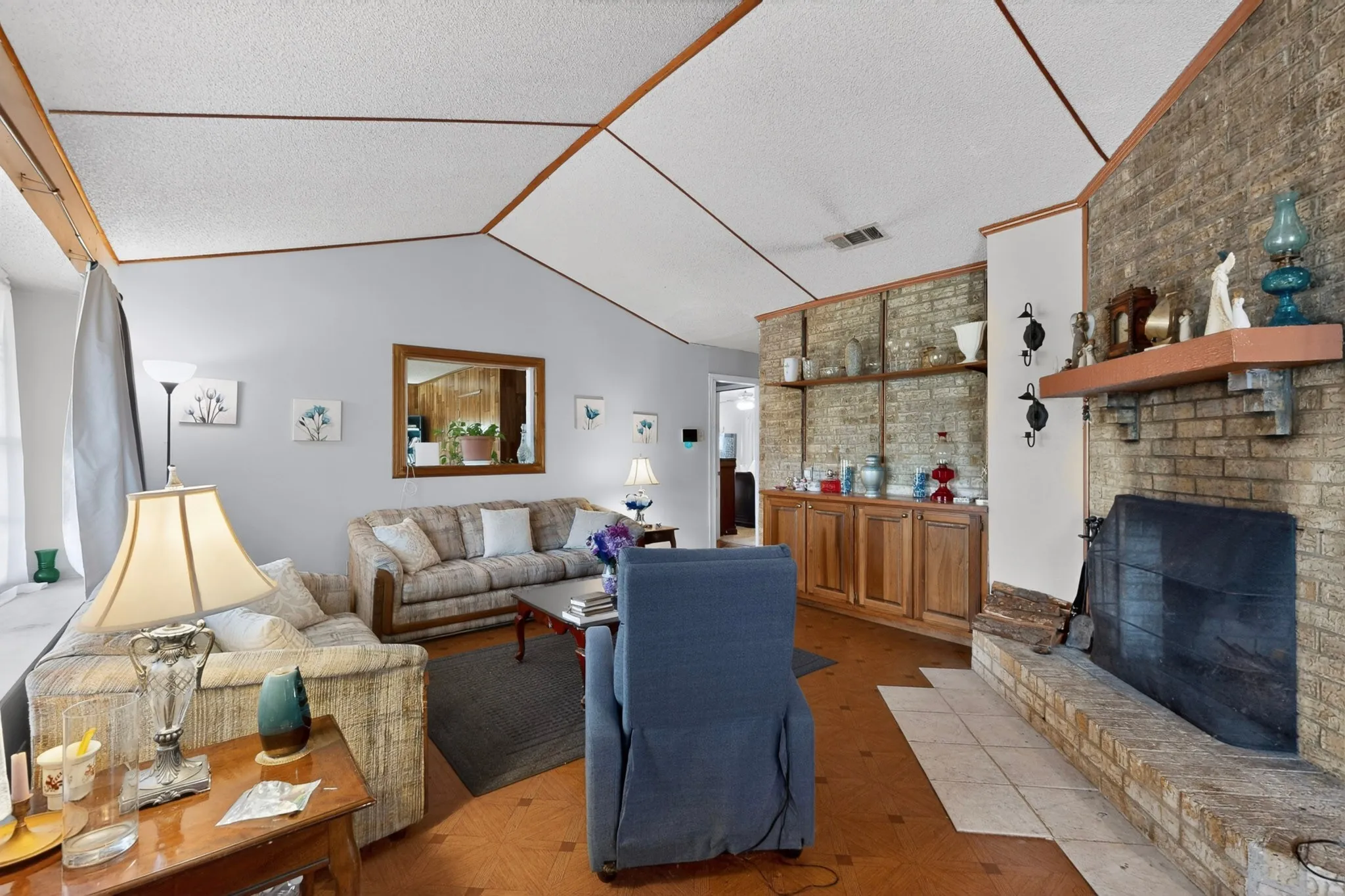 Living area featuring a brick fireplace with a wood mantle, vaulted ceilings, and built-in wood cabinetry with open shelving