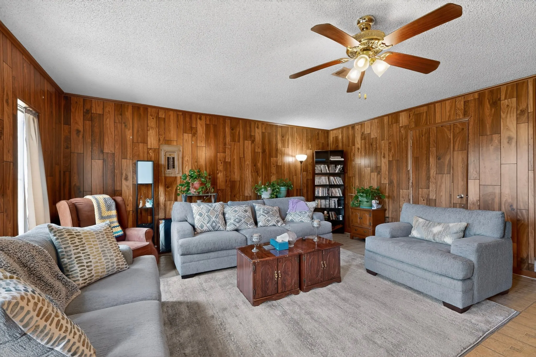 Room featuring full wood-paneled walls, a textured white ceiling, and a ceiling fan with integrated lighting