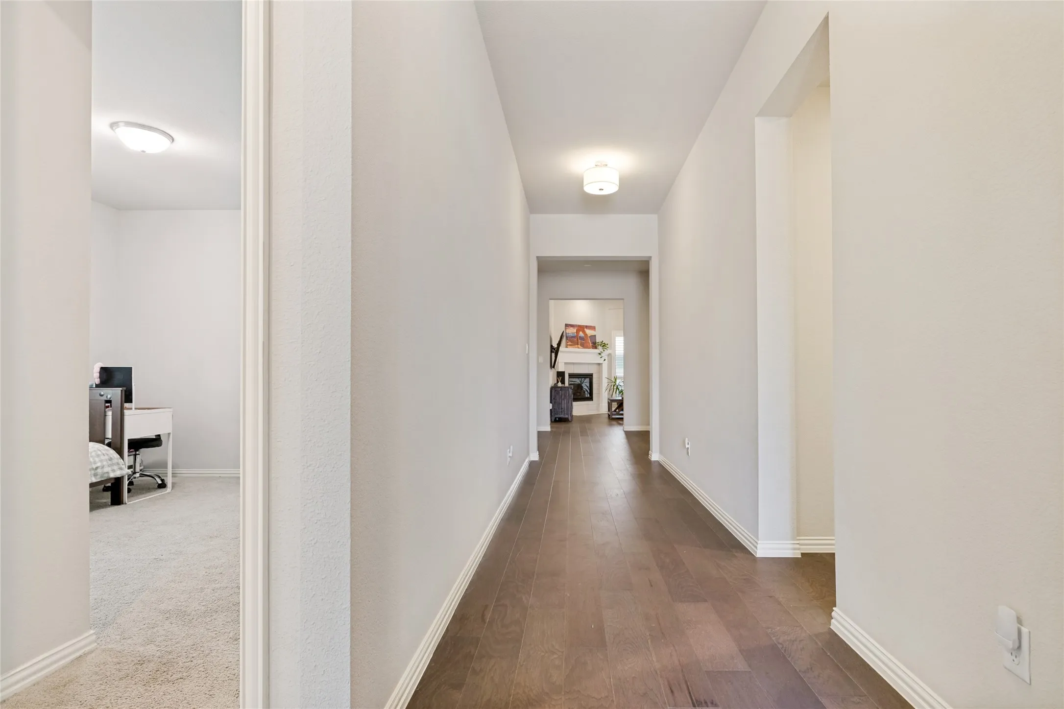 Wide hallway with wood-finish flooring, light neutral wall tones, and white baseboards
