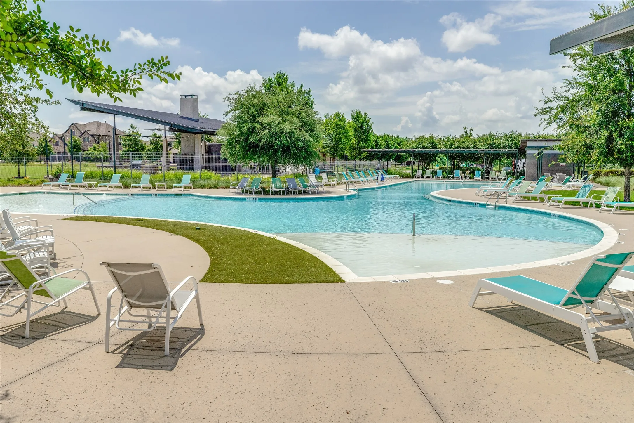 Resort-style swimming pool featuring a curved design, sun shelf, and surrounding concrete deck