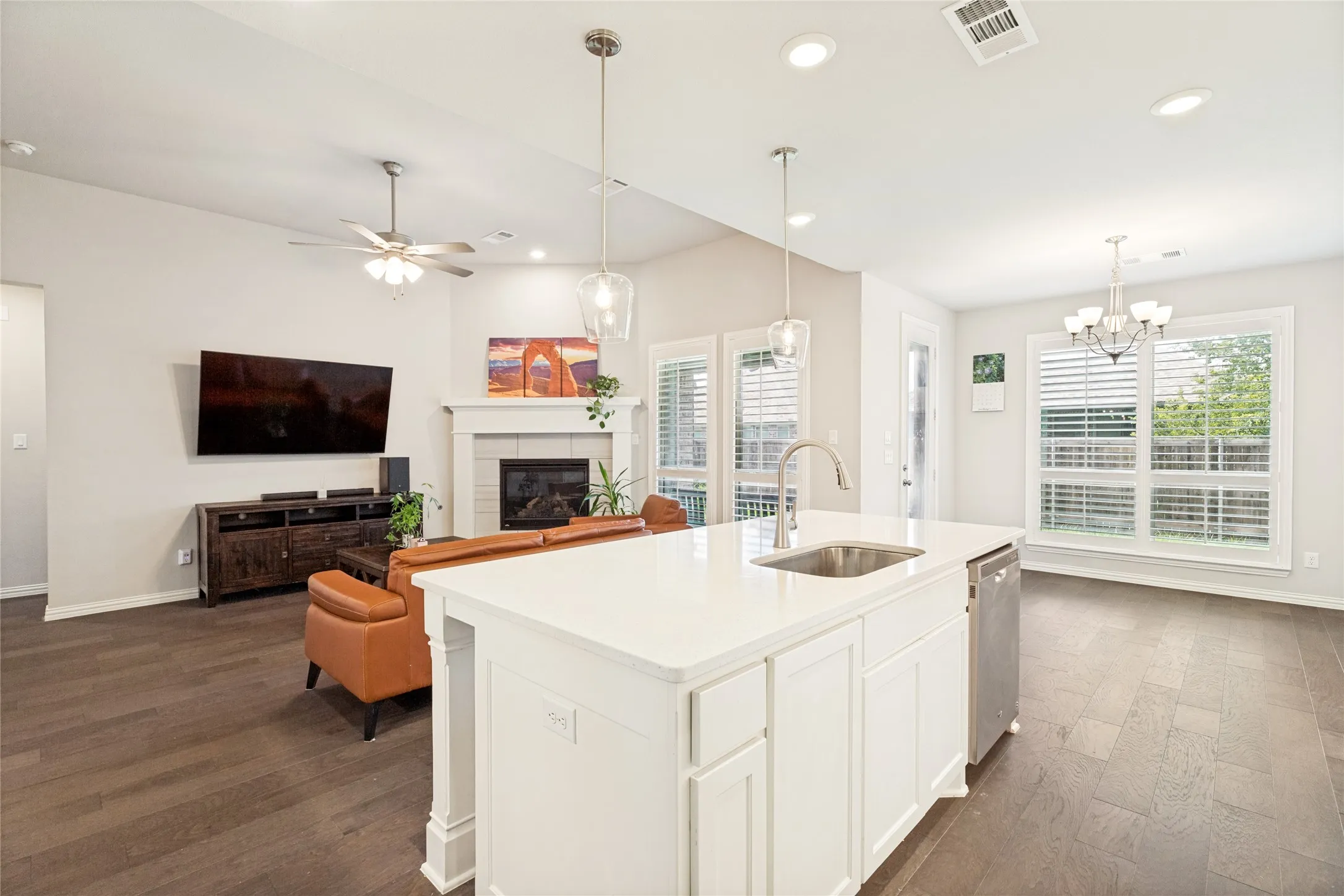 Open-concept kitchen featuring a white island with a stainless steel sink, built-in dishwasher, and two pendant lights
