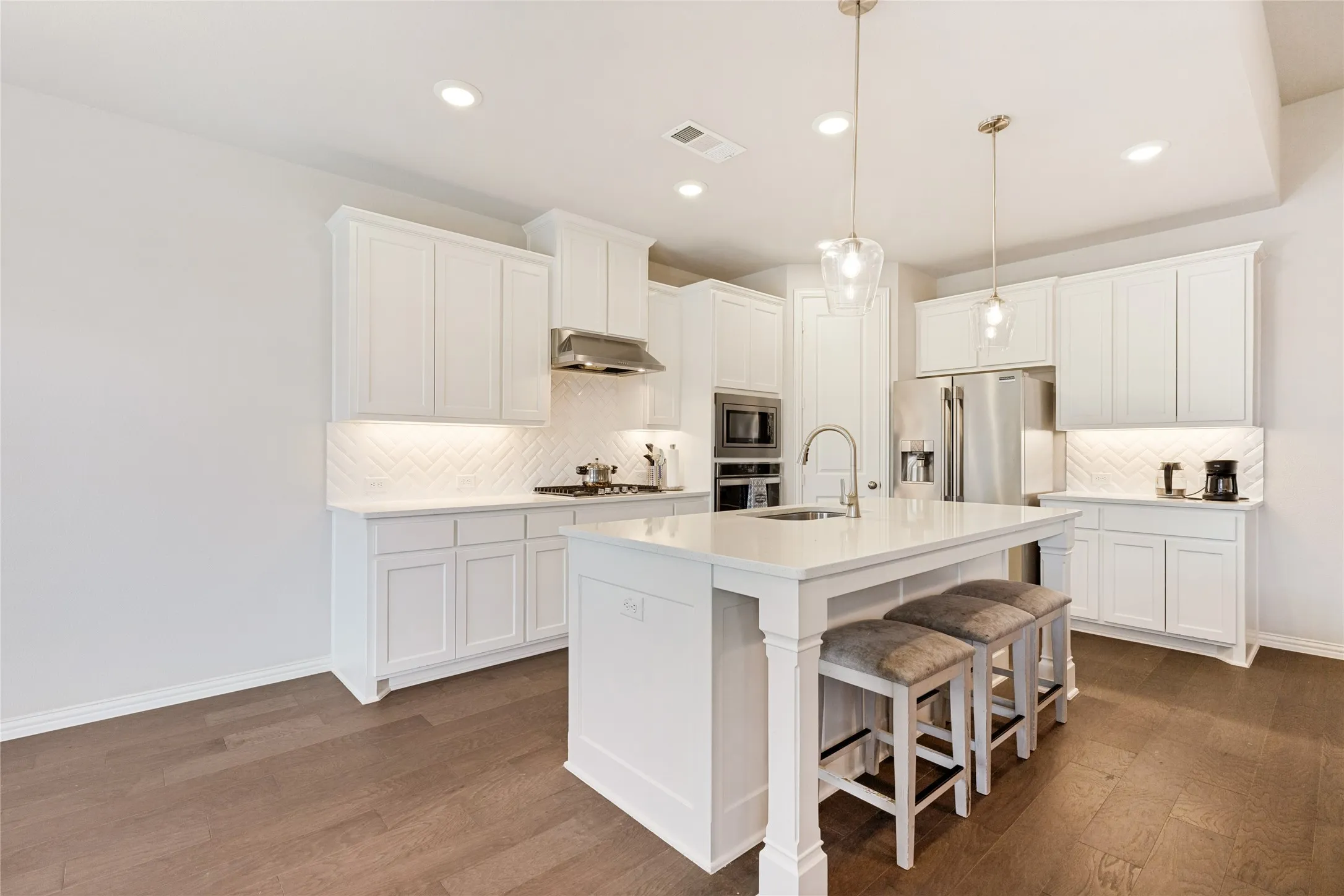 Modern kitchen featuring an island with built-in seating, white cabinetry, integrated stainless steel appliances, pendant lighting, and wood-finish flooring