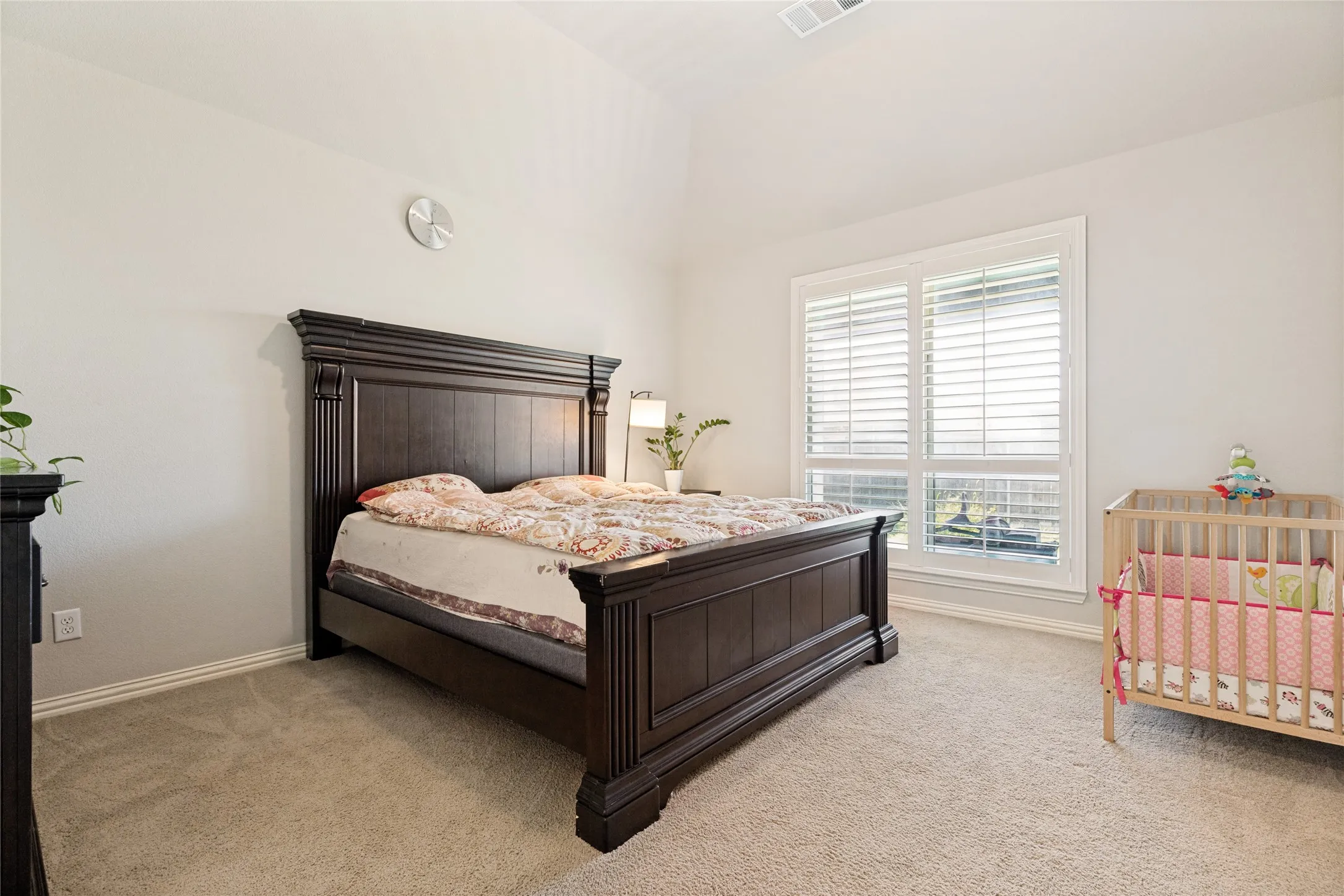 Carpeted room featuring a large window with white plantation shutters, vaulted ceiling, and neutral wall paint