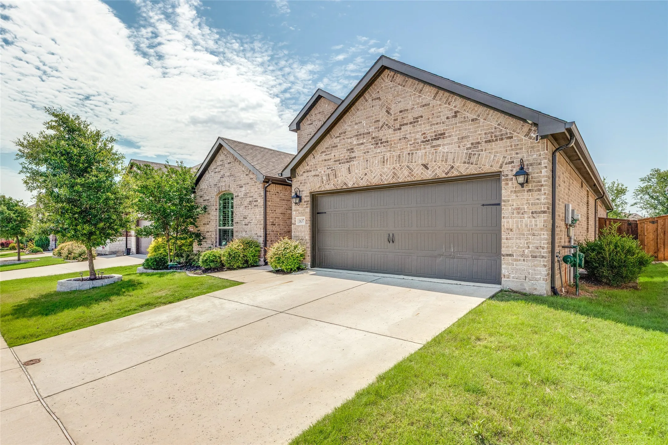Brick exterior featuring a two-car garage with overhead lighting, a concrete driveway, and established landscaping