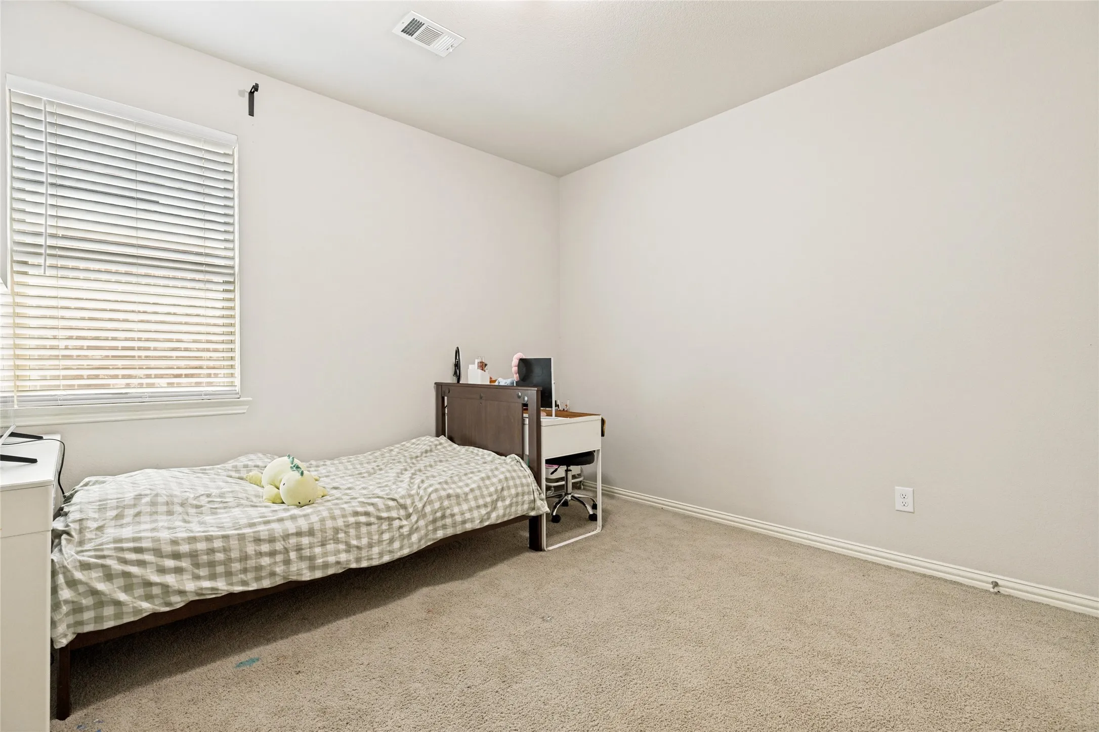 Neutral wall color with carpeted flooring, featuring a window with horizontal blinds and a ceiling vent