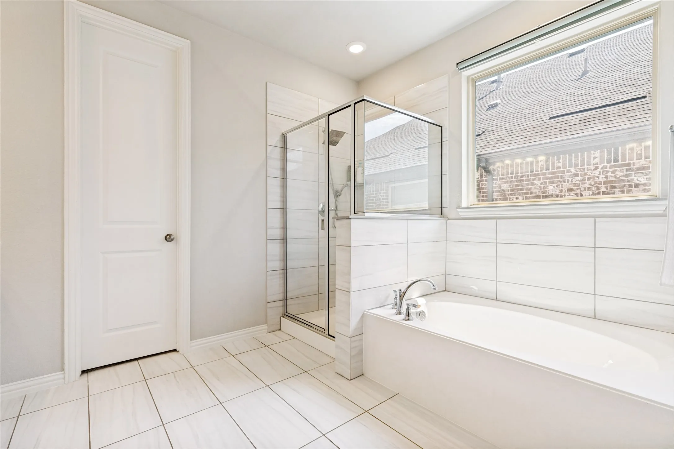 White tiled bathroom featuring a built-in soaking tub with chrome fixtures, a glass-enclosed shower, large format floor tiles, recessed lighting, and a window with blinds