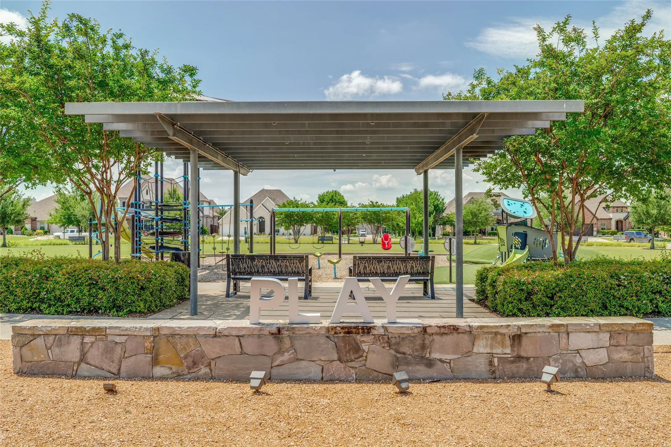 Community playground featuring a metal pergola, stone-clad seating wall, and integrated benches