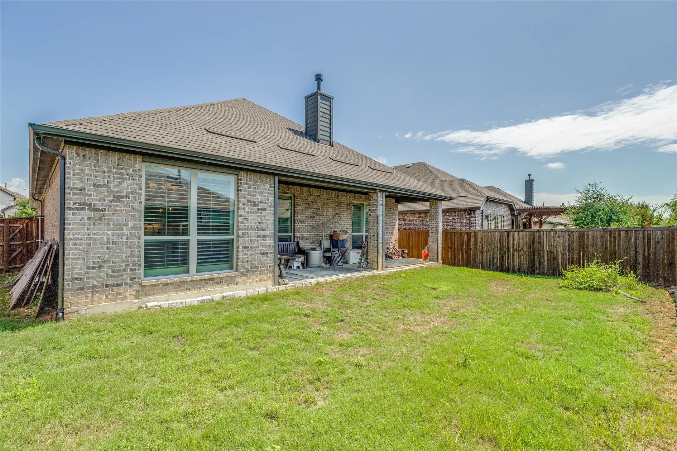 Expansive backyard featuring a covered patio, brick exterior, and a privacy fence