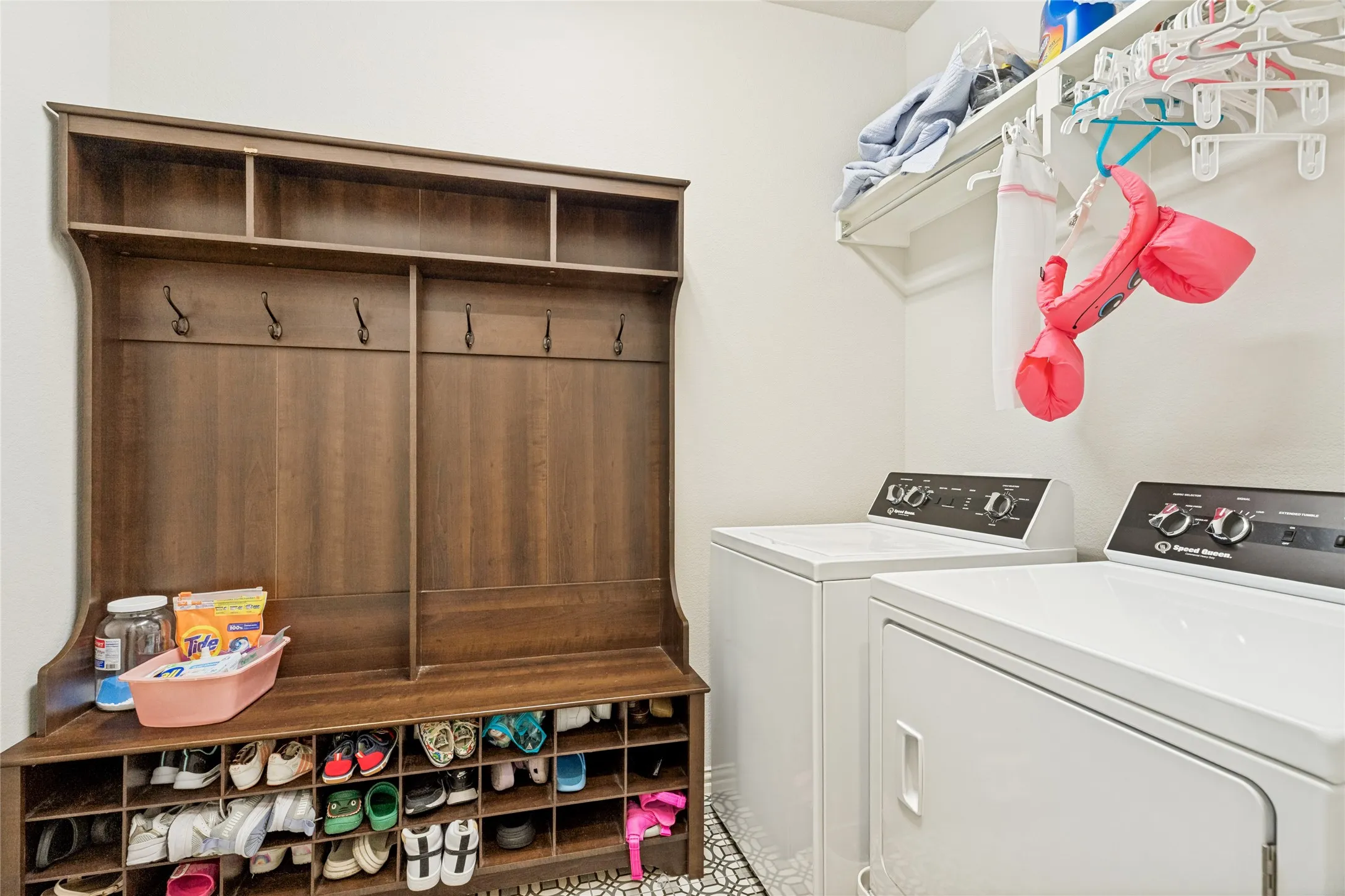 Dedicated utility room featuring a built-in wood-finish mudroom bench with storage, multiple coat hooks, and upper shelving