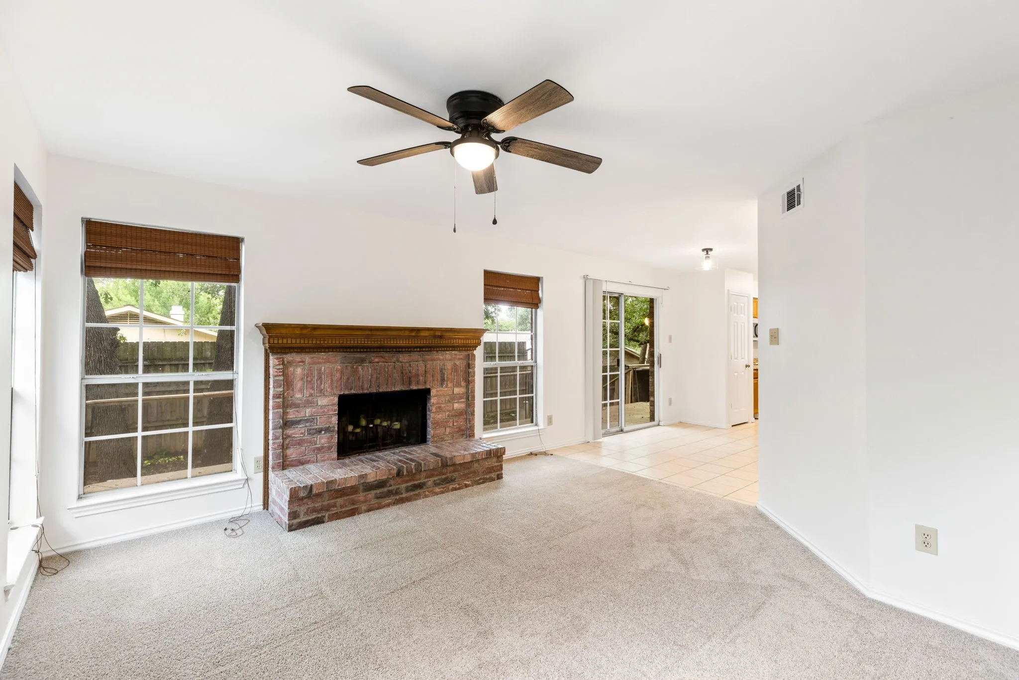 Living space featuring a brick fireplace with a wood mantle, light-toned carpeting, and a ceiling fan with integrated lighting