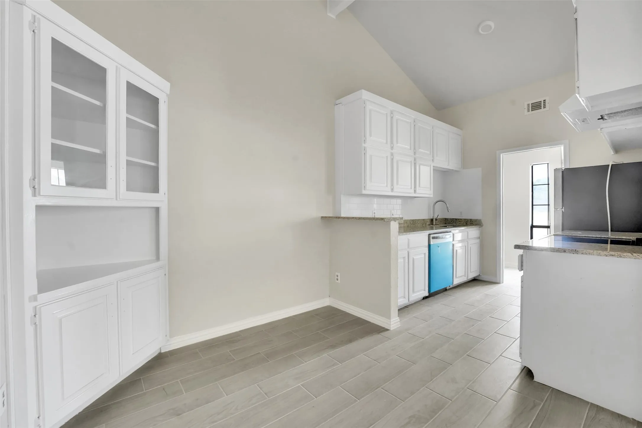 Kitchen featuring freestanding refrigerator, dishwashing machine, white cabinets, high vaulted ceiling, and light stone counters