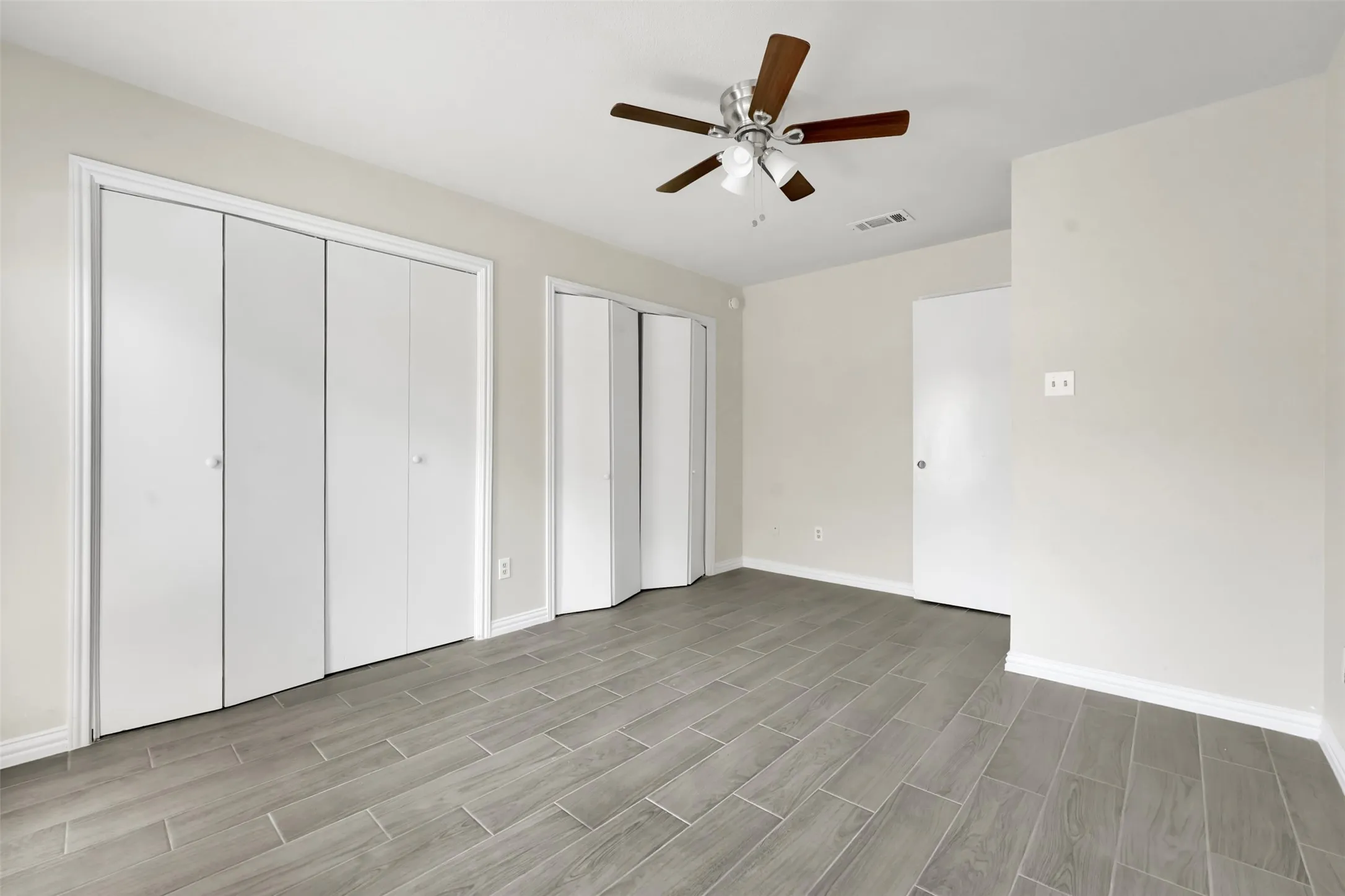 Unfurnished bedroom featuring multiple closets, wood finished floors, and ceiling fan