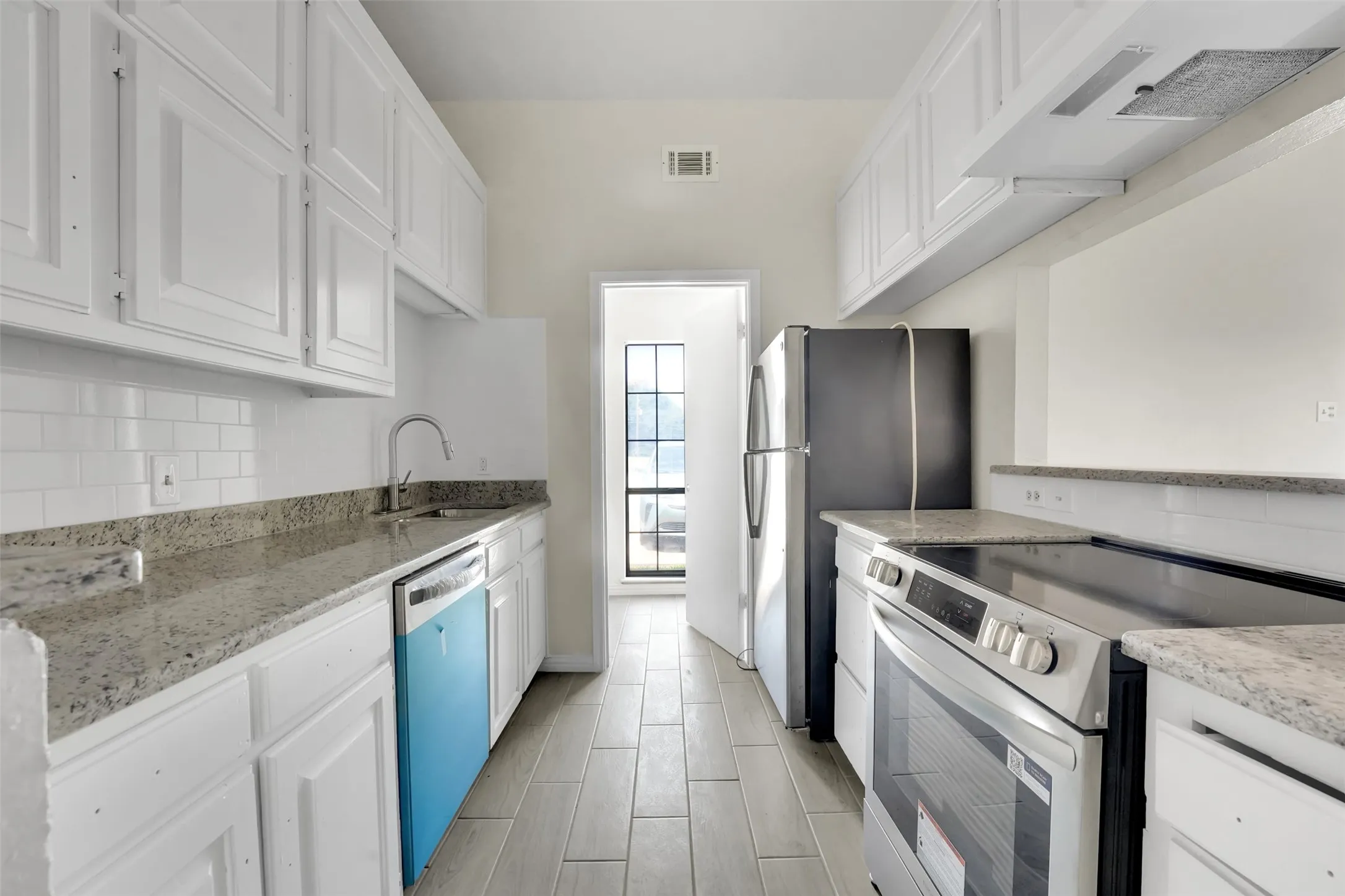 Kitchen with appliances with stainless steel finishes, white cabinets, wall chimney range hood, tasteful backsplash, and light stone countertops