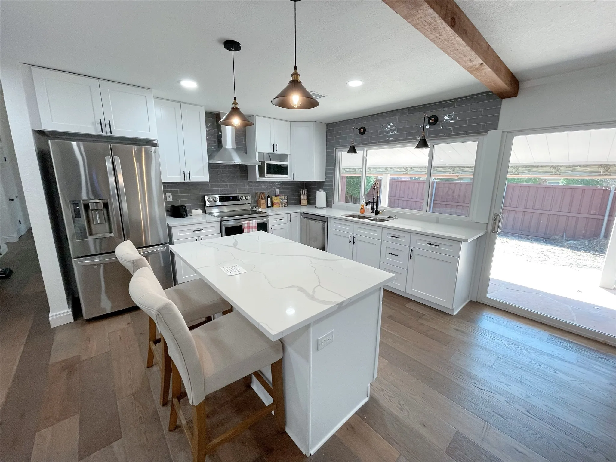 Modern kitchen featuring a central island with a quartz countertop, white shaker-style cabinetry, stainless steel appliances, and wood-finish flooring