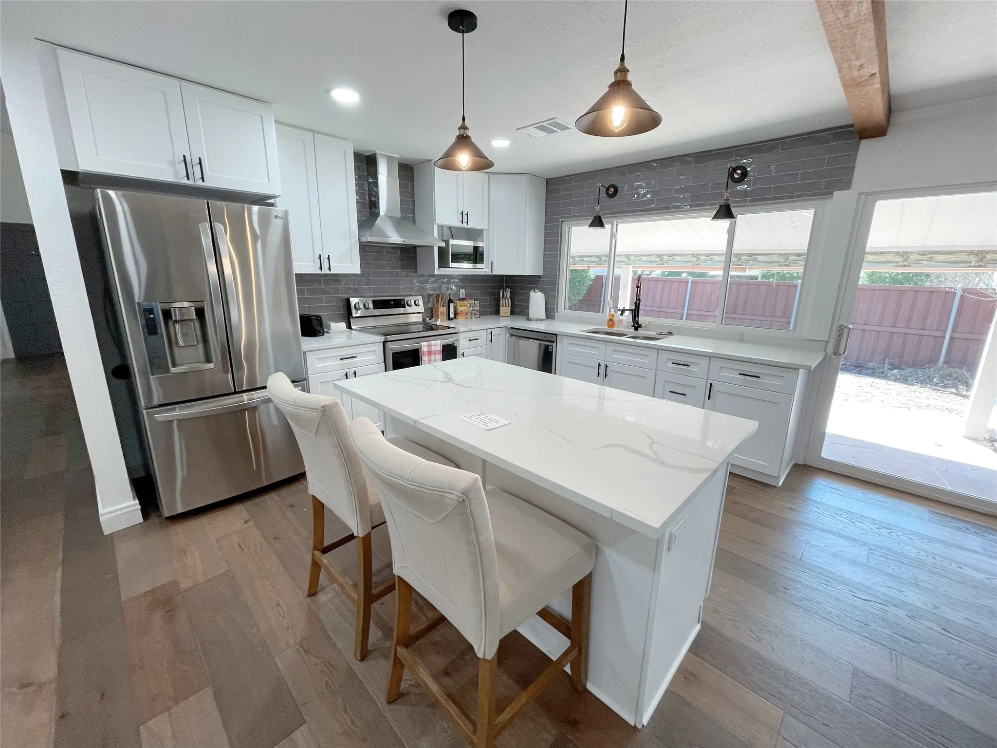 Modern kitchen featuring a central island with a quartz countertop, stainless steel appliances, white cabinetry, and wood-finish flooring