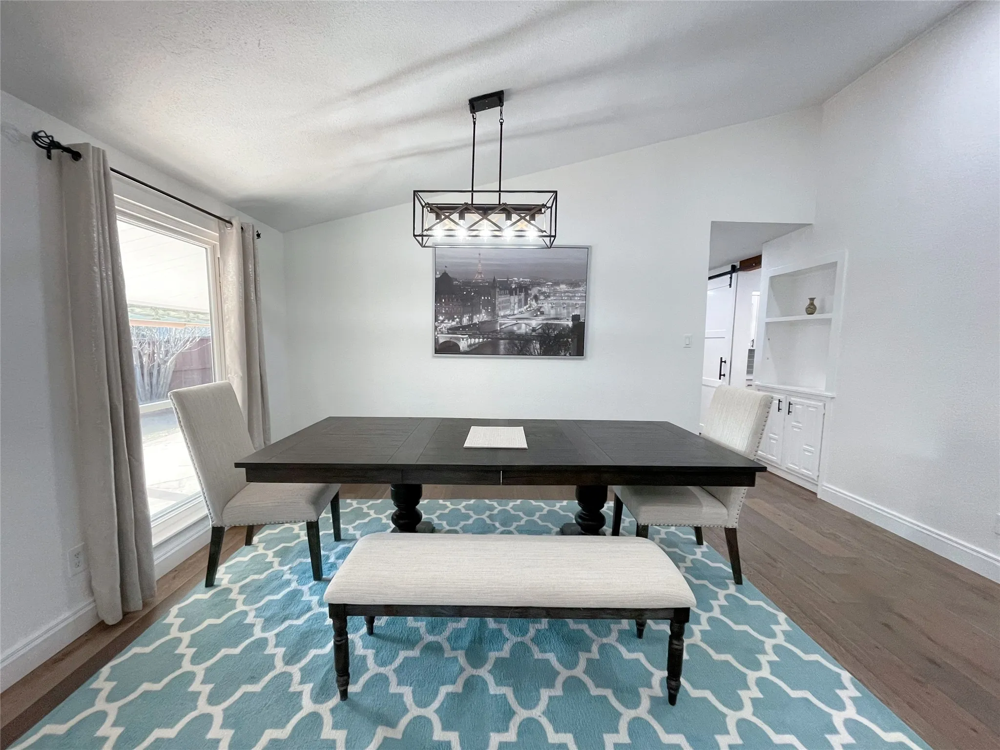 Vaulted ceiling dining area featuring a modern linear chandelier, wood-finish flooring, and a built-in display cabinet