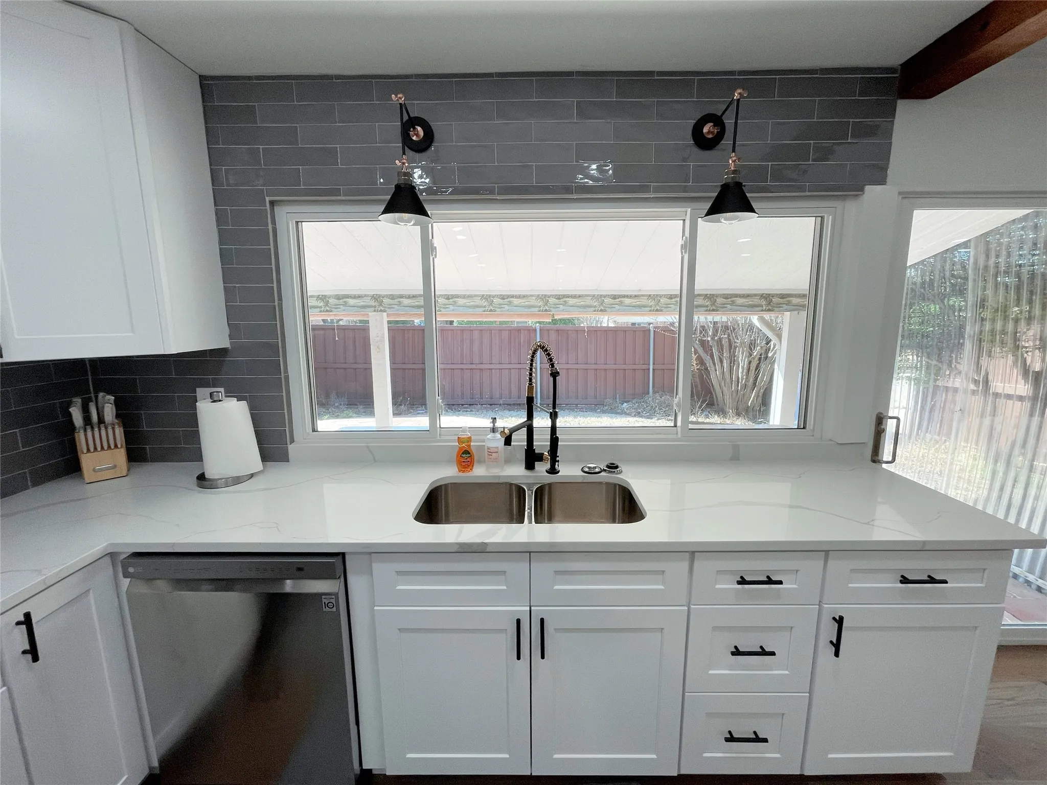 Bright kitchen featuring white shaker cabinetry, stainless steel dishwasher, dual basin sink with a matte black faucet, and a grey subway tile backsplash