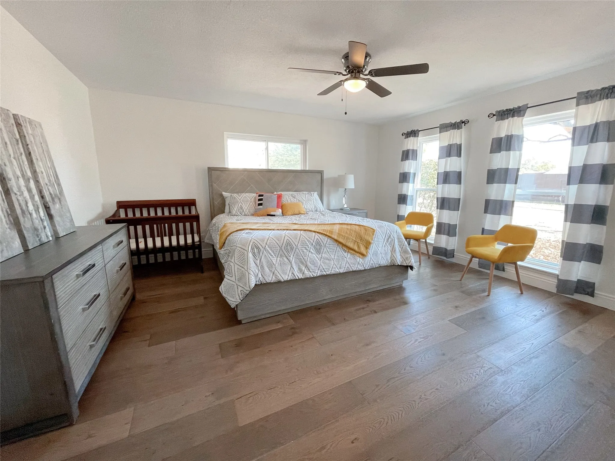 Spacious room featuring wood-finish flooring, multiple windows, a ceiling fan with integrated lighting, and white baseboards