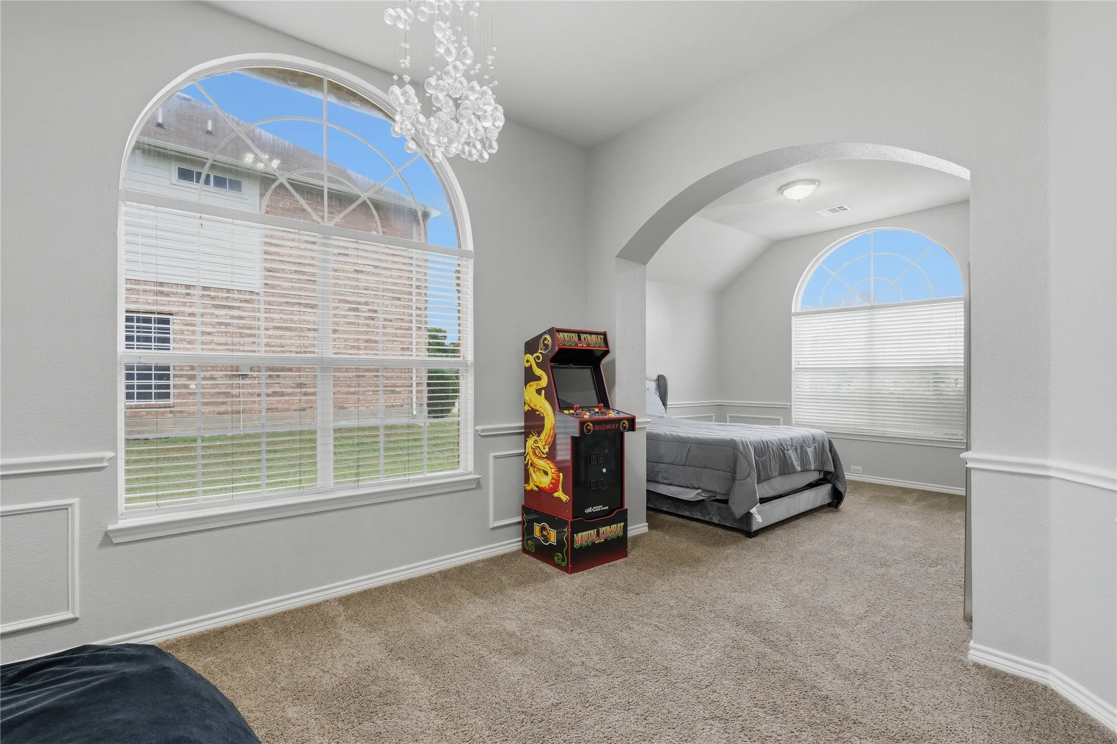 Light-filled interior space featuring a large arched window with transom detailing, textured carpet flooring, decorative wall paneling, and an arched entryway to an additional room with a similar arched window
