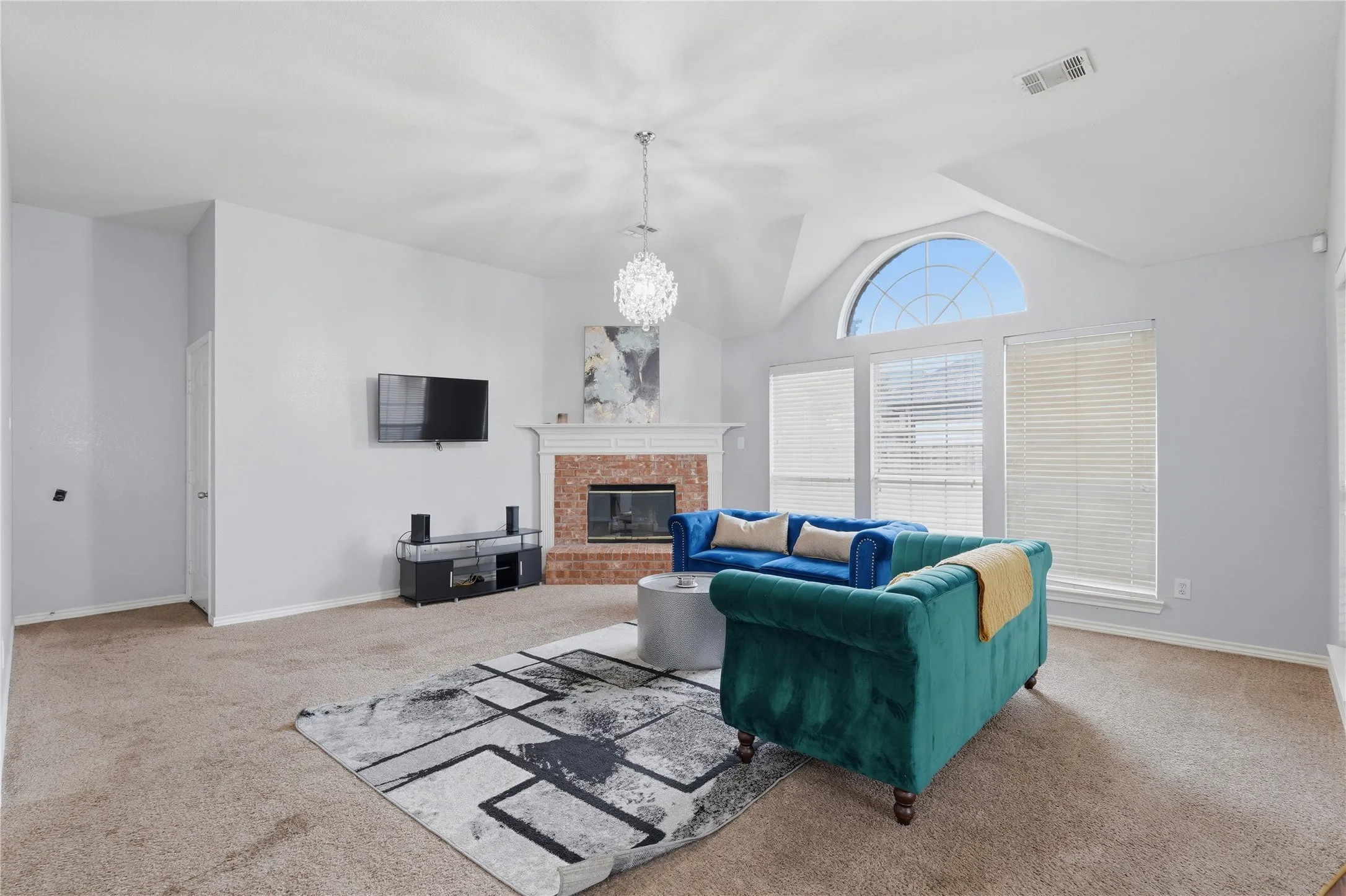 Living area featuring a brick fireplace with a white mantel, vaulted ceilings, and a large arched window above three rectangular windows