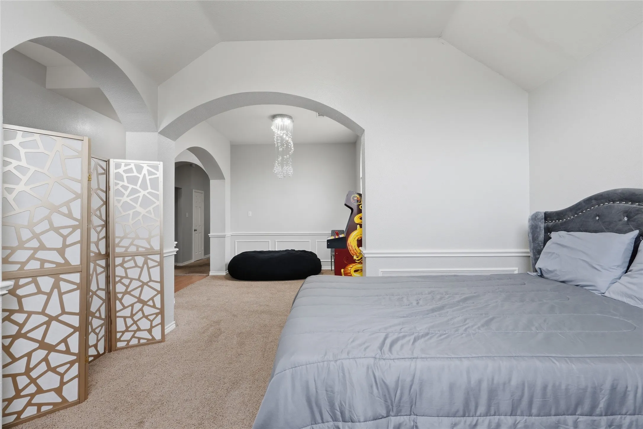 Vaulted ceiling room with arched doorways, carpet flooring, decorative wall paneling, and a unique crystal chandelier