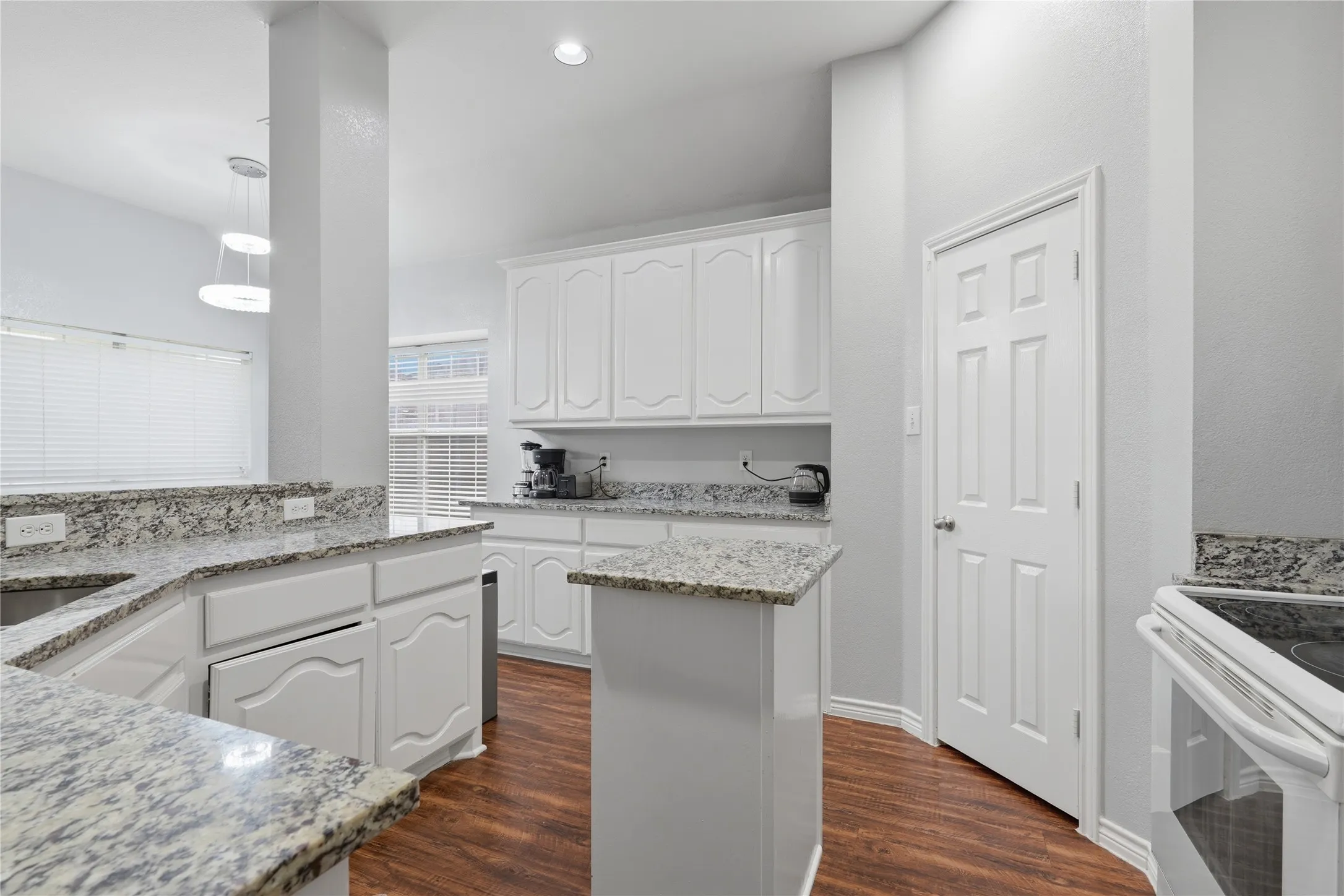 Kitchen featuring white cabinetry, light-toned granite countertops, wood-finish flooring, and a built-in electric range