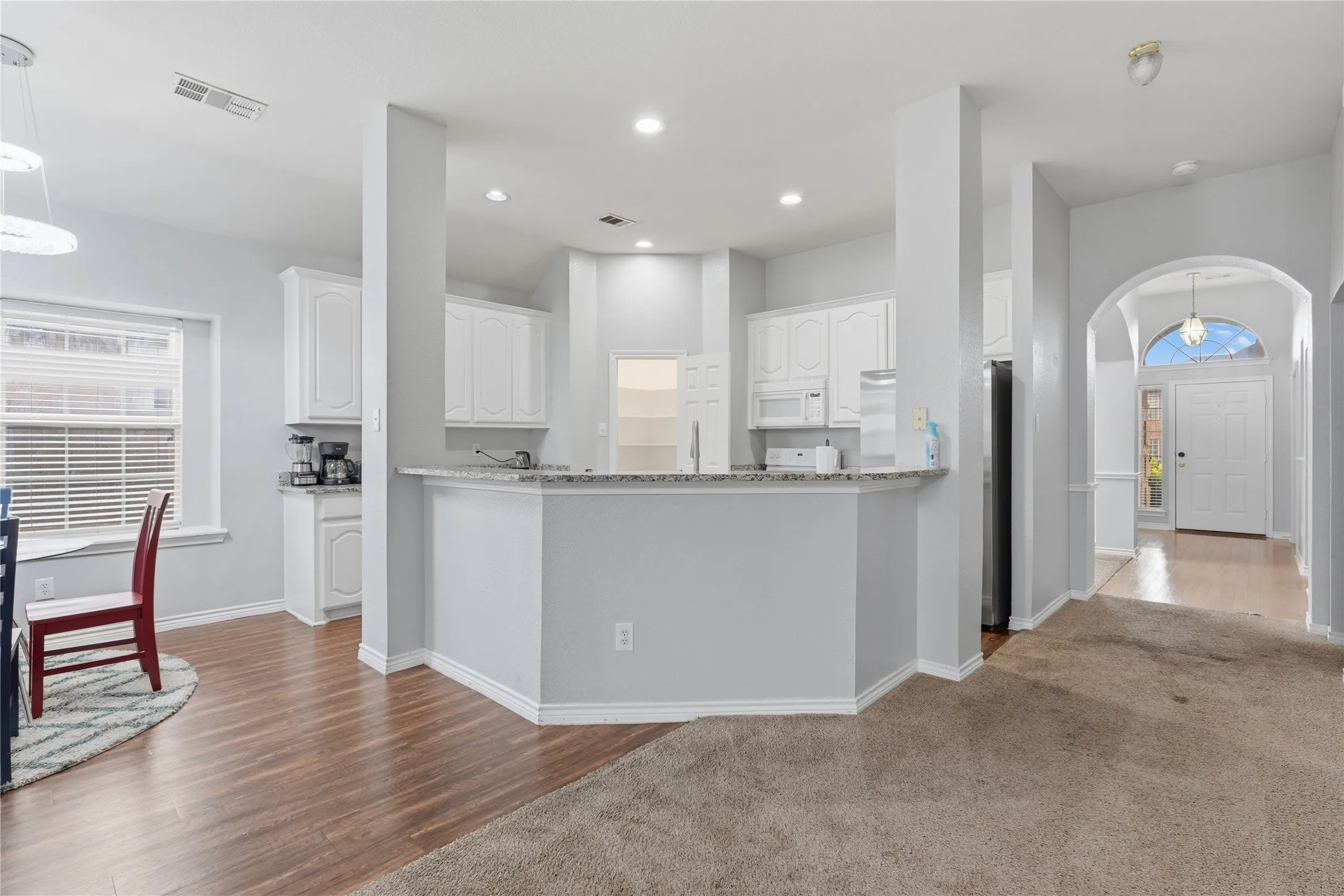 Open-concept kitchen featuring white cabinetry, granite countertops, and built-in appliances