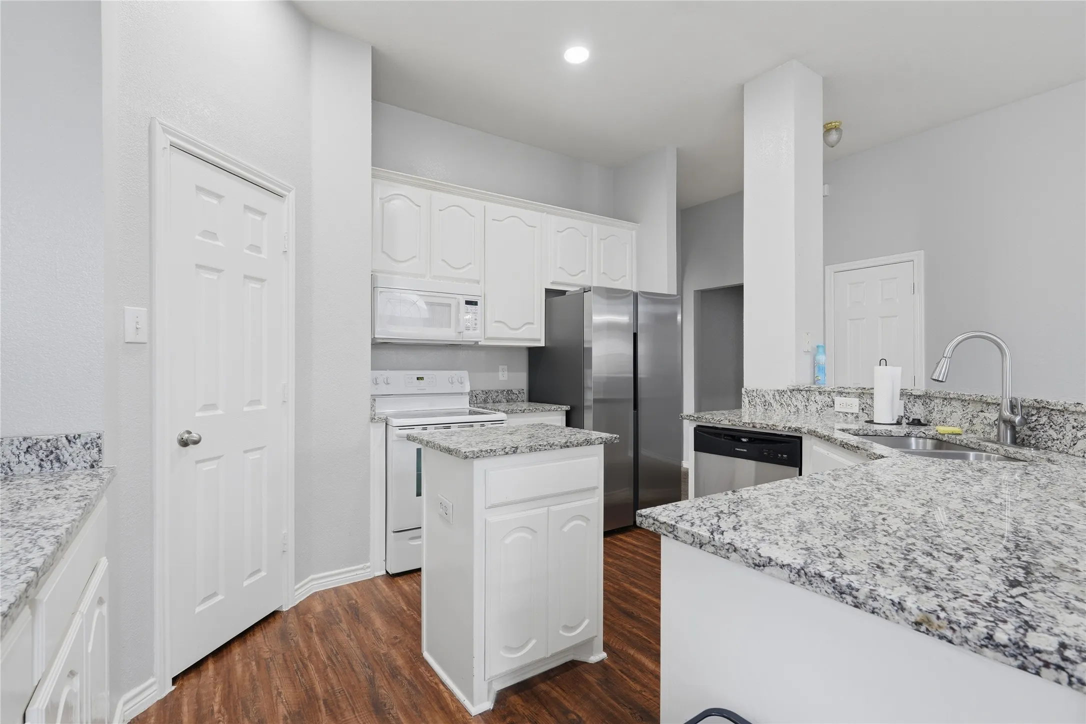 Kitchen featuring wood-finish flooring, white cabinetry, integrated stainless steel appliances, and a central island with a granite countertop