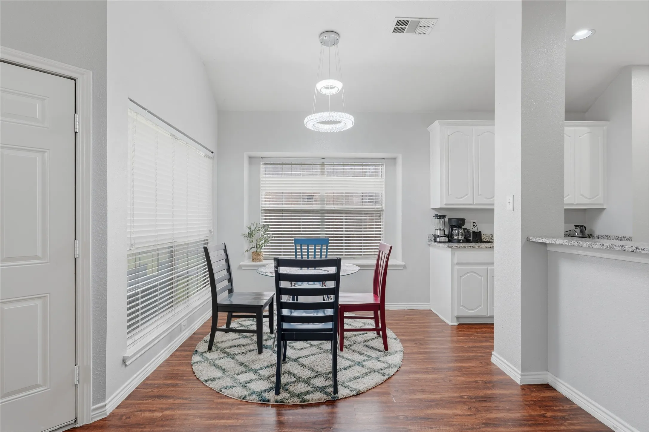 Dining area featuring wood-finish flooring, a wall of windows with blinds, and a contemporary chandelier