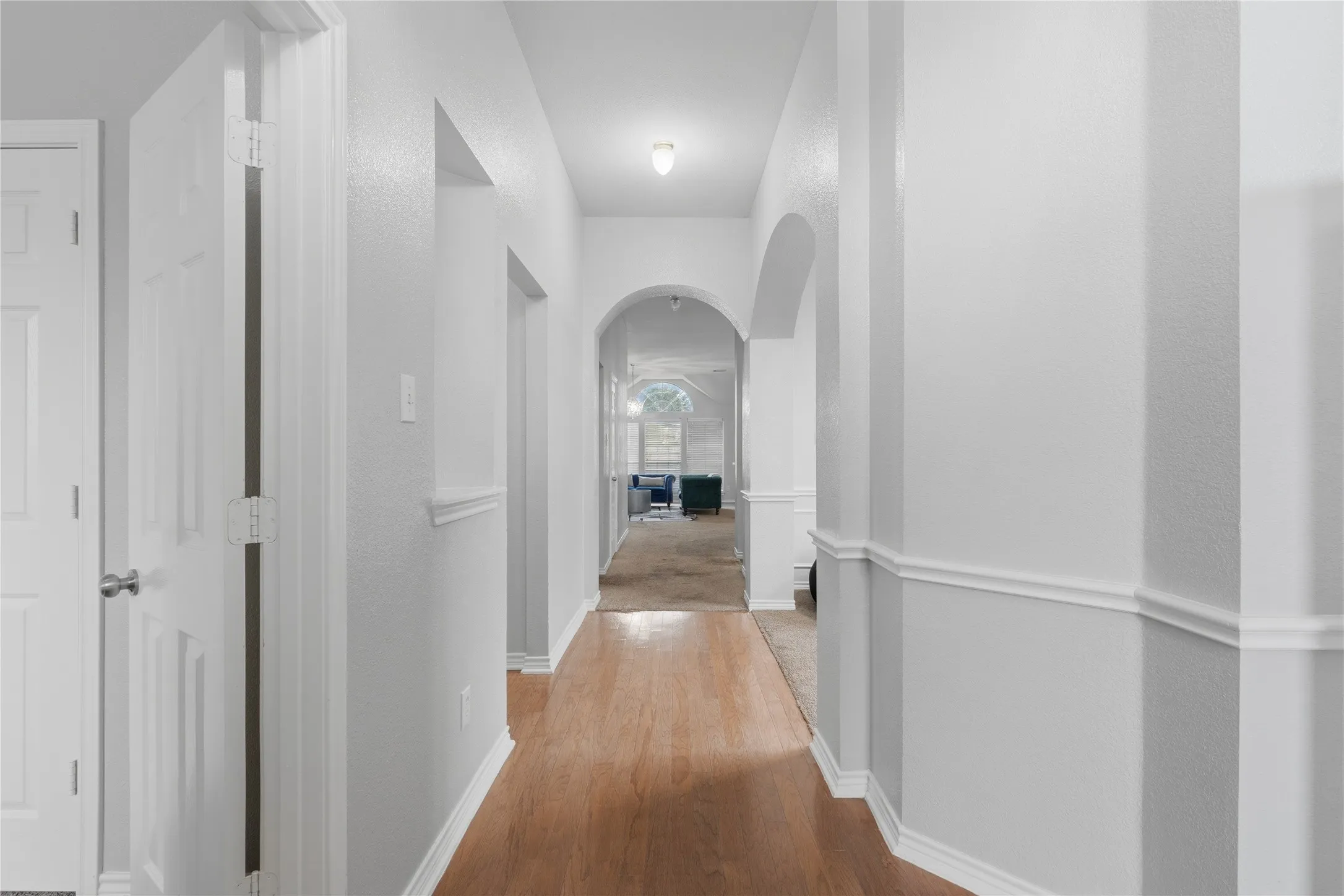 Hallway featuring wood-finish flooring, light gray walls, white trim, and a decorative archway
