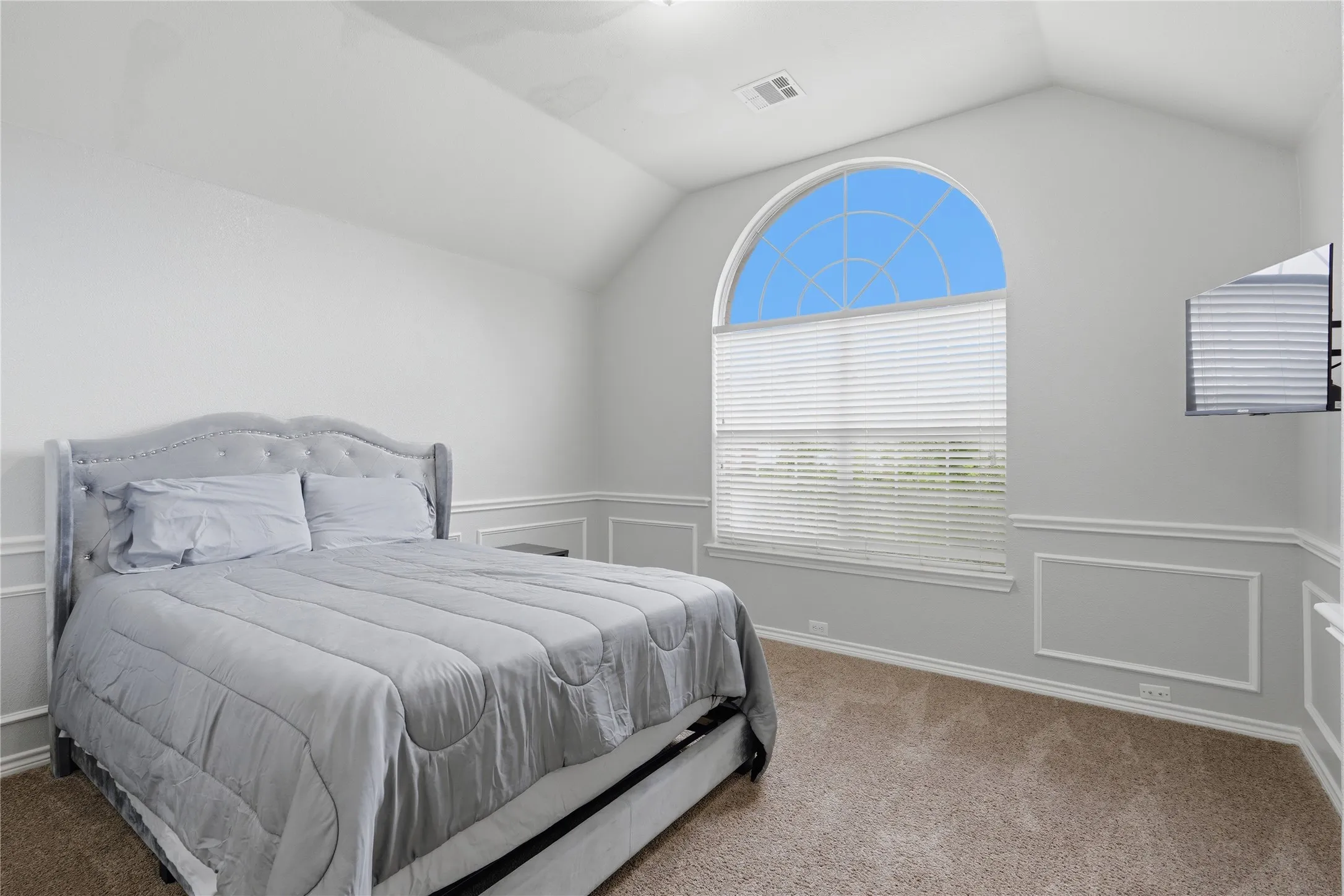 Vaulted ceiling room featuring a large arched window with horizontal blinds, neutral carpet flooring, and decorative wall molding