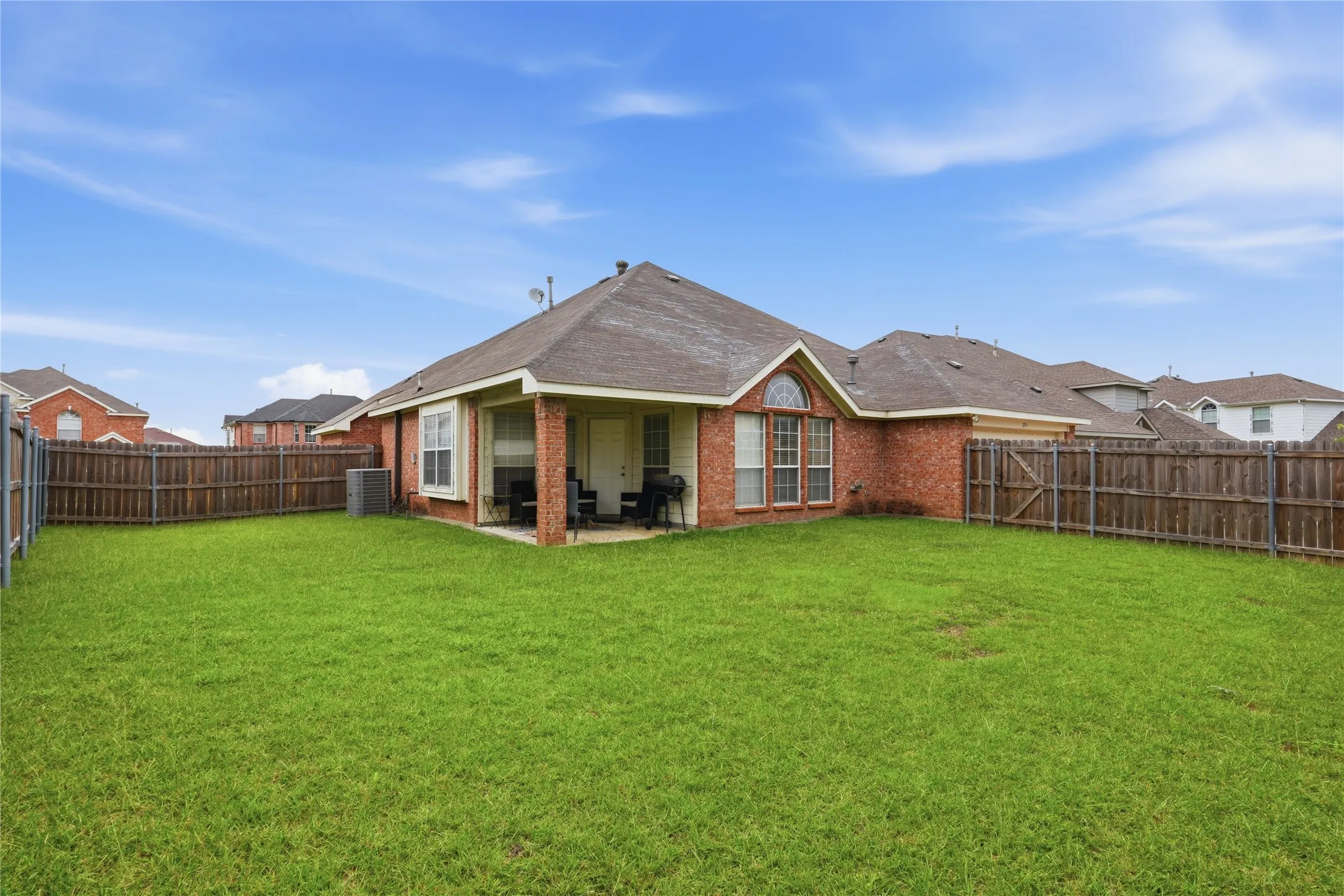 Expansive backyard featuring a manicured lawn, full privacy fencing, and a covered patio
