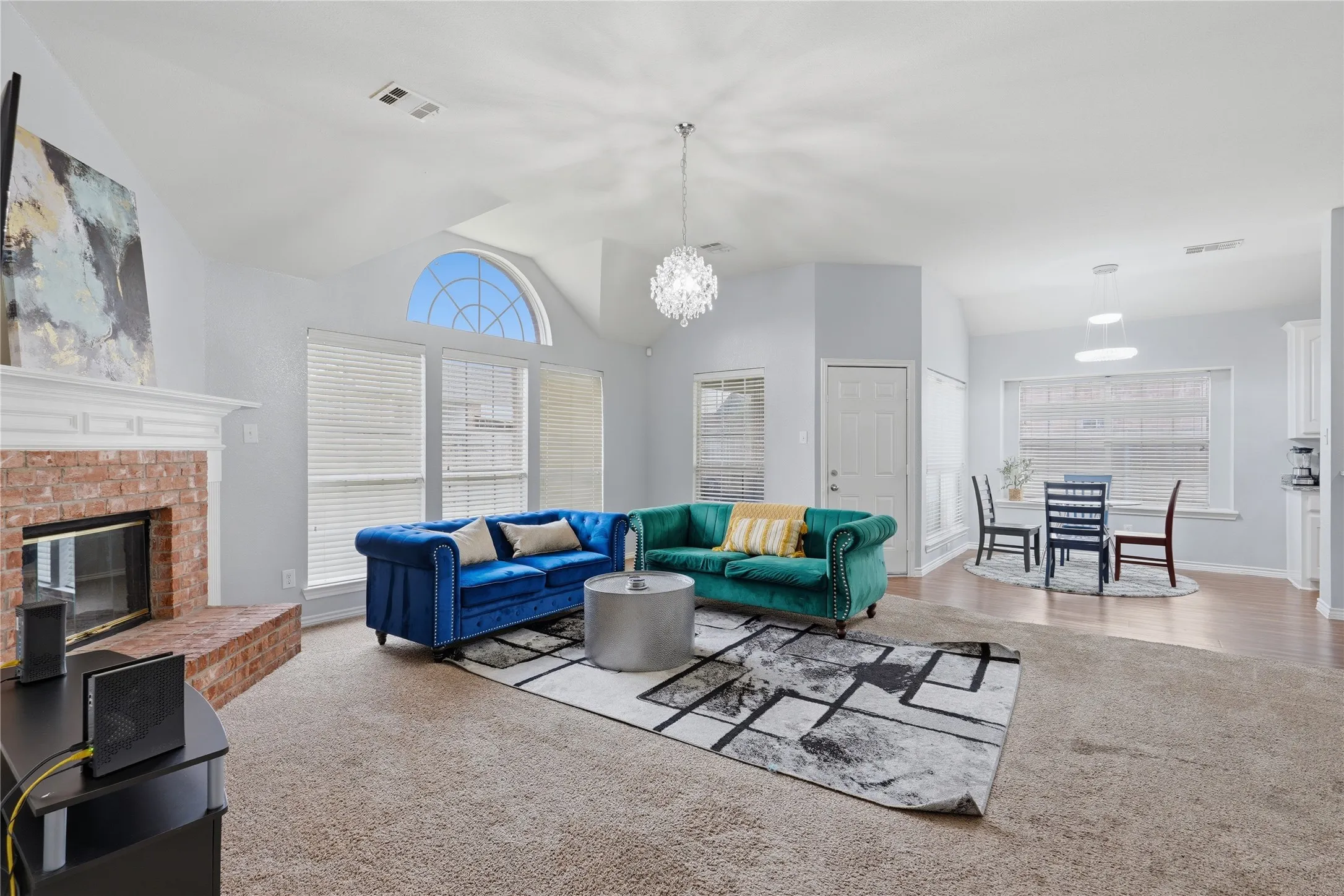 Spacious living area featuring a brick fireplace with a white mantel, vaulted ceilings, and a large arched window