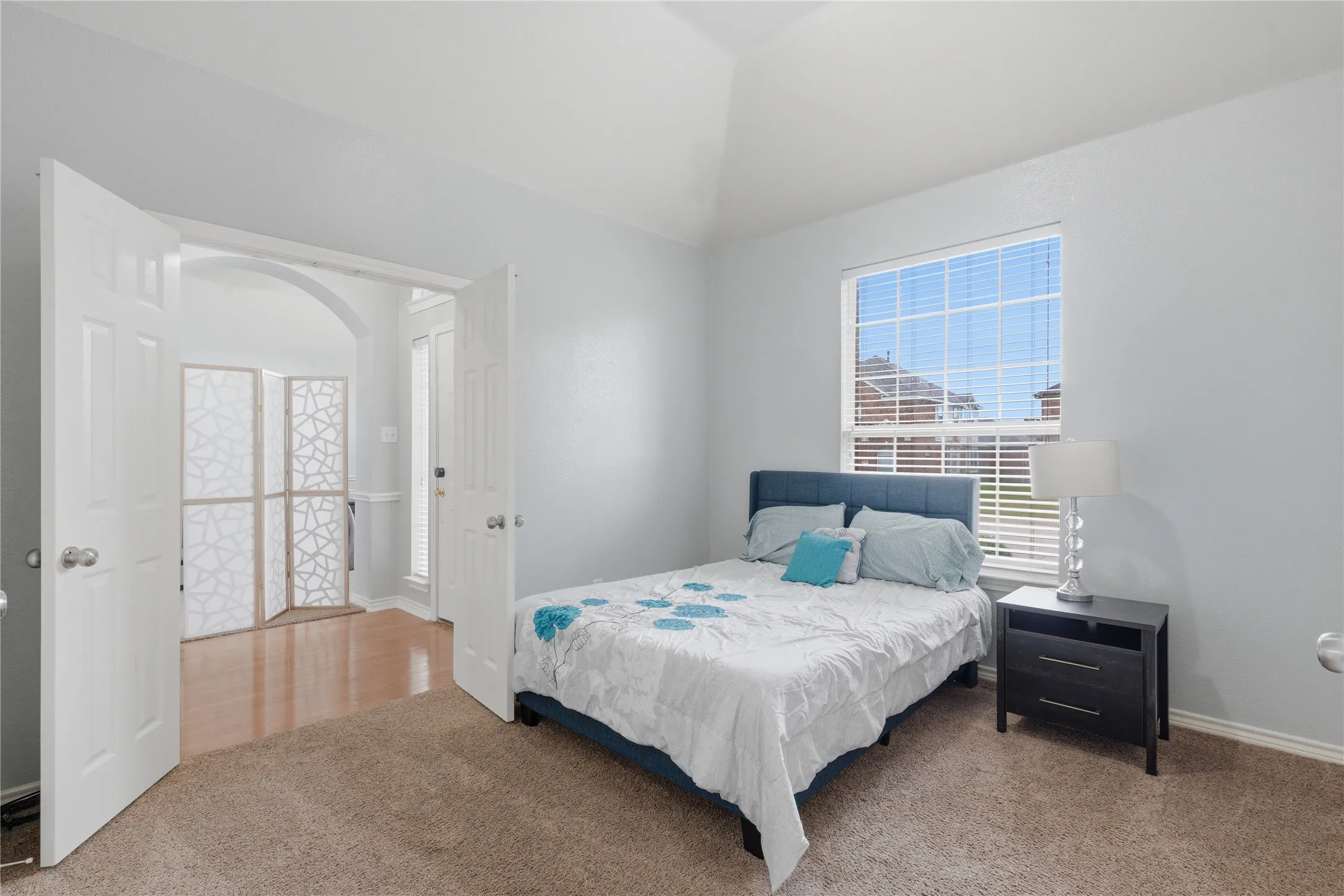 Vaulted ceiling room with broad window, light-toned walls, and carpet flooring