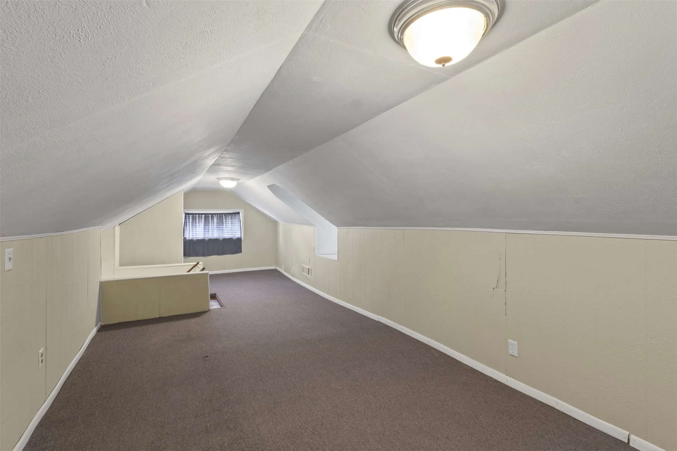 Carpeted attic space featuring sloped ceilings, two flush-mount ceiling lights, light-toned wall paneling, and a window with blinds