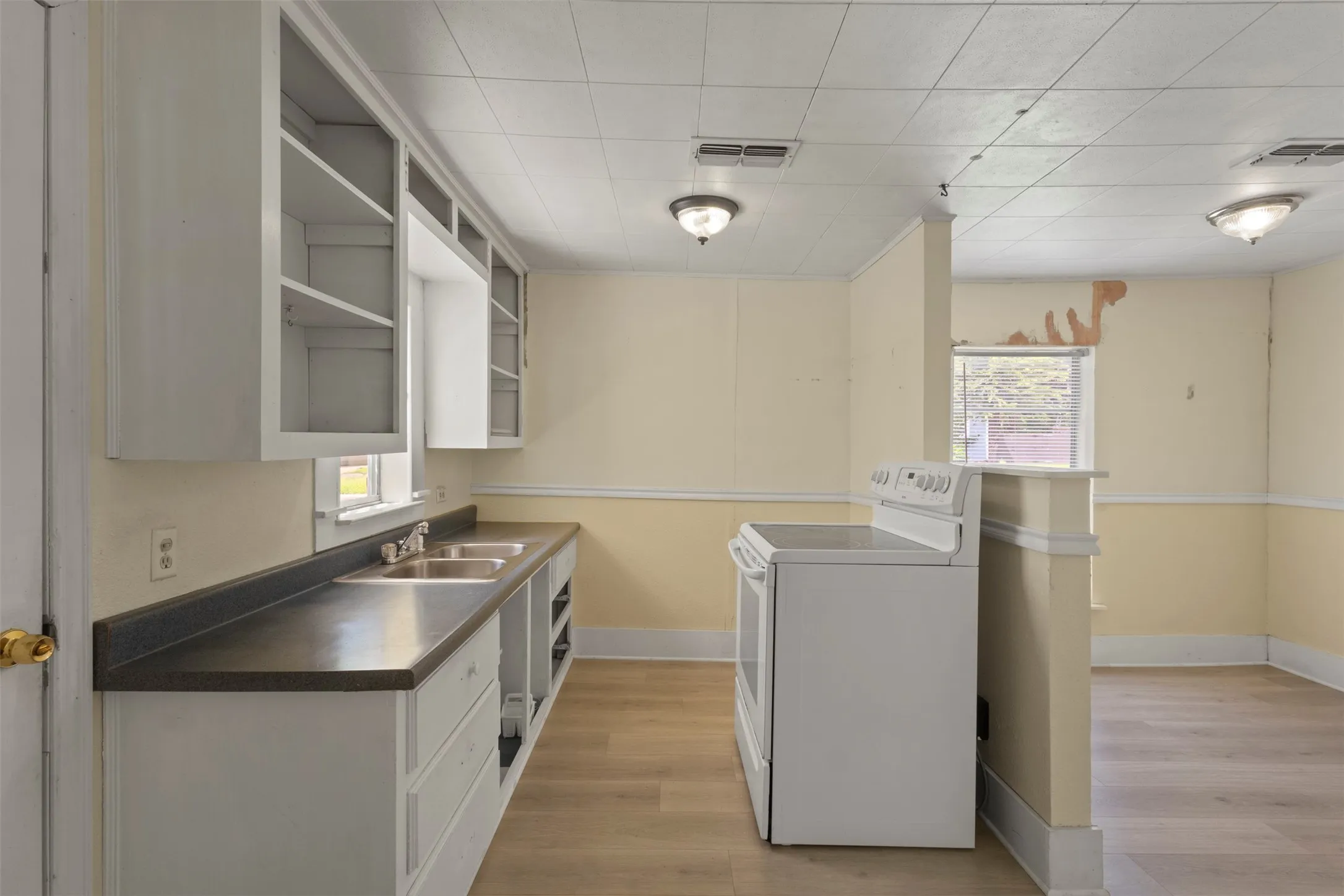 Kitchen area featuring light wood-finish flooring, white cabinetry, a double basin stainless steel sink, and a white electric range