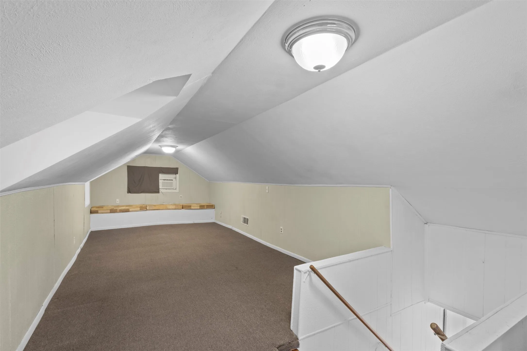 Finished attic space featuring brown carpeting, light beige wall panels, a built-in window air conditioning unit, and a built-in wood-finish bench
